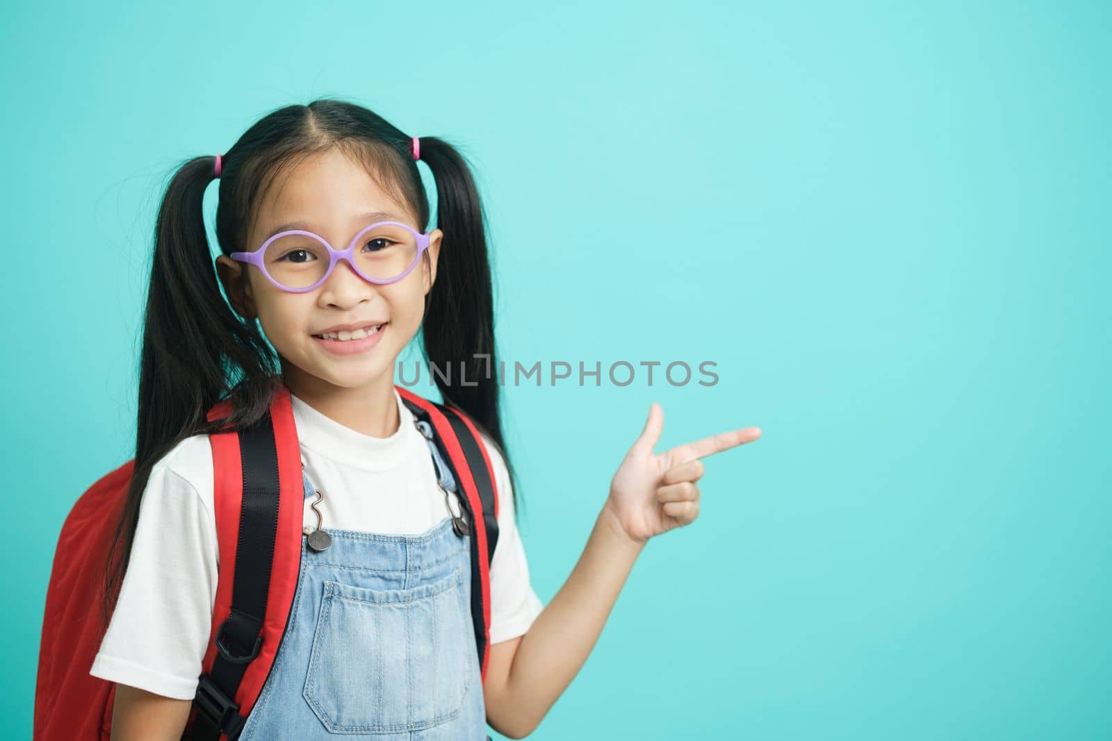 Close-up kid schoolgirl Pointing Fingers At Copy Space, she nice cute attractive cheerful amazed glad pointing one fingers looking aside copy space isolated on blue pastel background isolated on blue pastel background. Educational concept for school