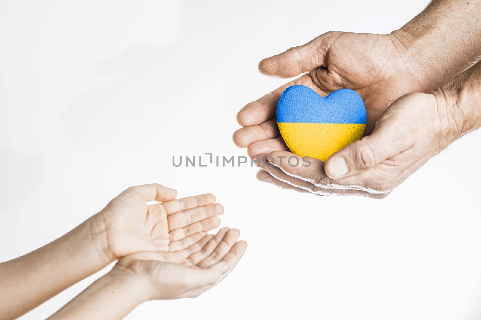old hands give painted yellow and blue heart to chldrens hands on white background. concept needs help and support, truth will win