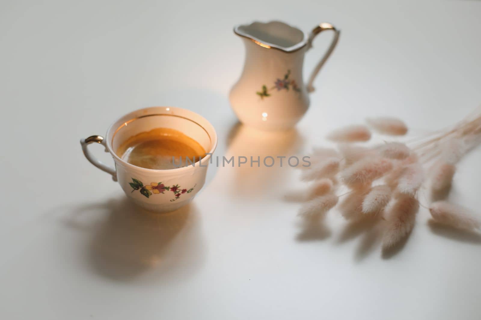 cup with coffee and milk jug on a white wooden background, closeup. Energy breakfast, morning routine concept by paralisart