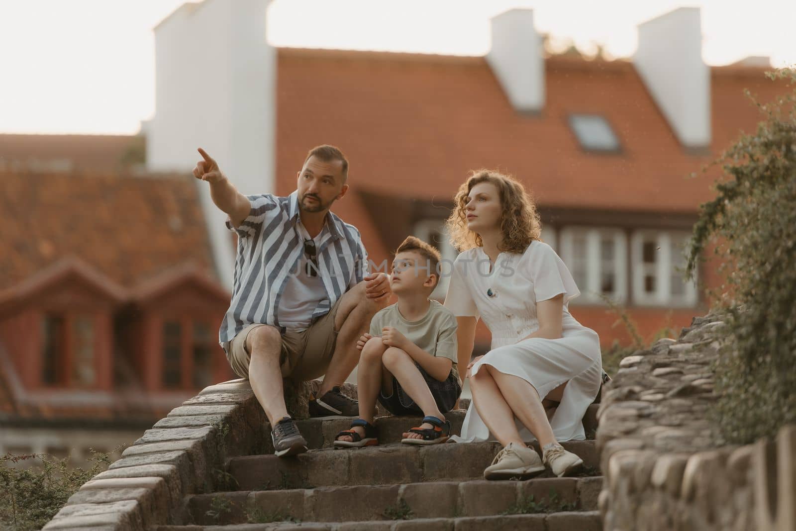 A family is speaking on the stairs between roofs in an old European town. A happy father, mother, and son are having fun in the evening.