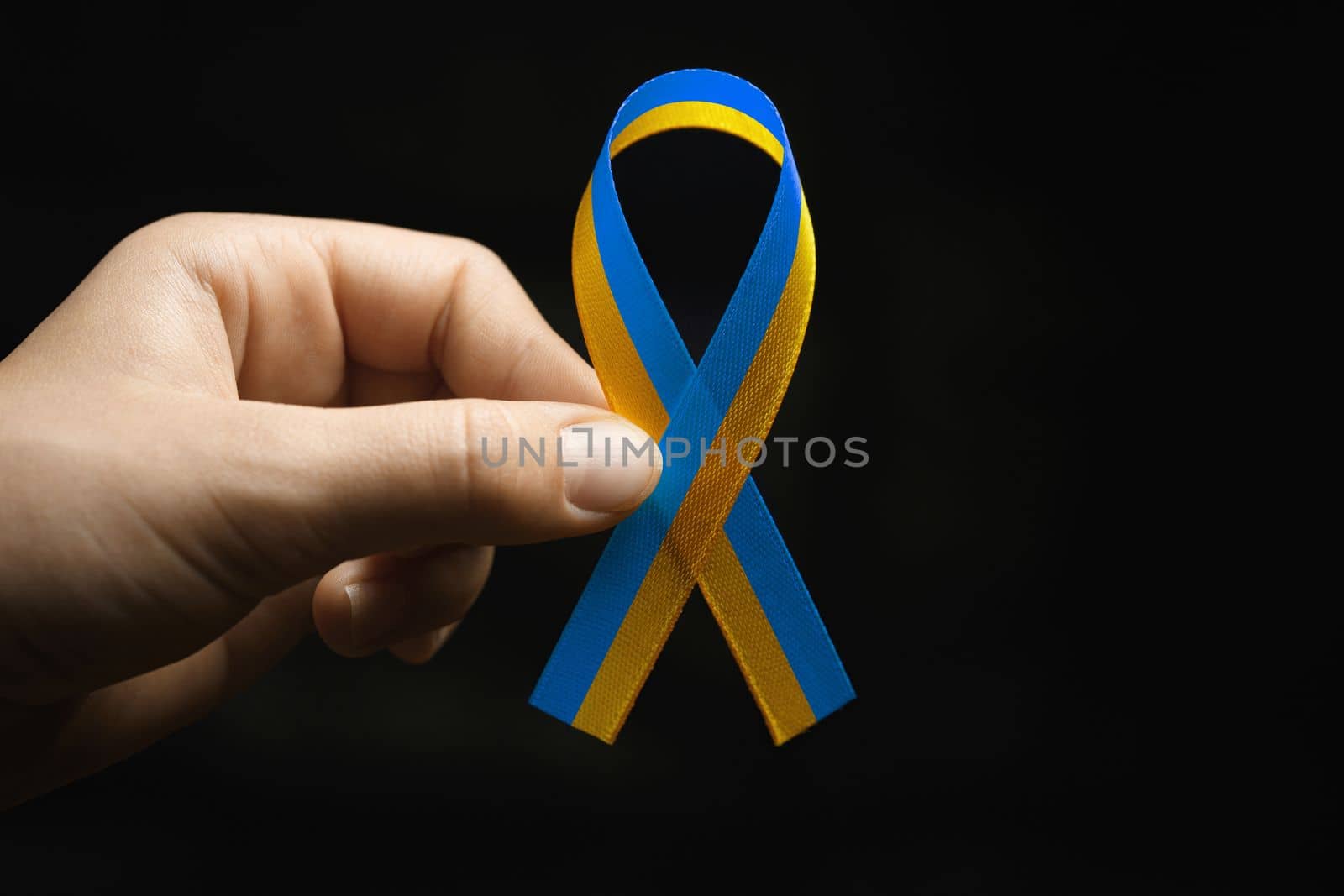 blue and yellow ribbon in female hands on dark background. concept needs help and support, truth will win