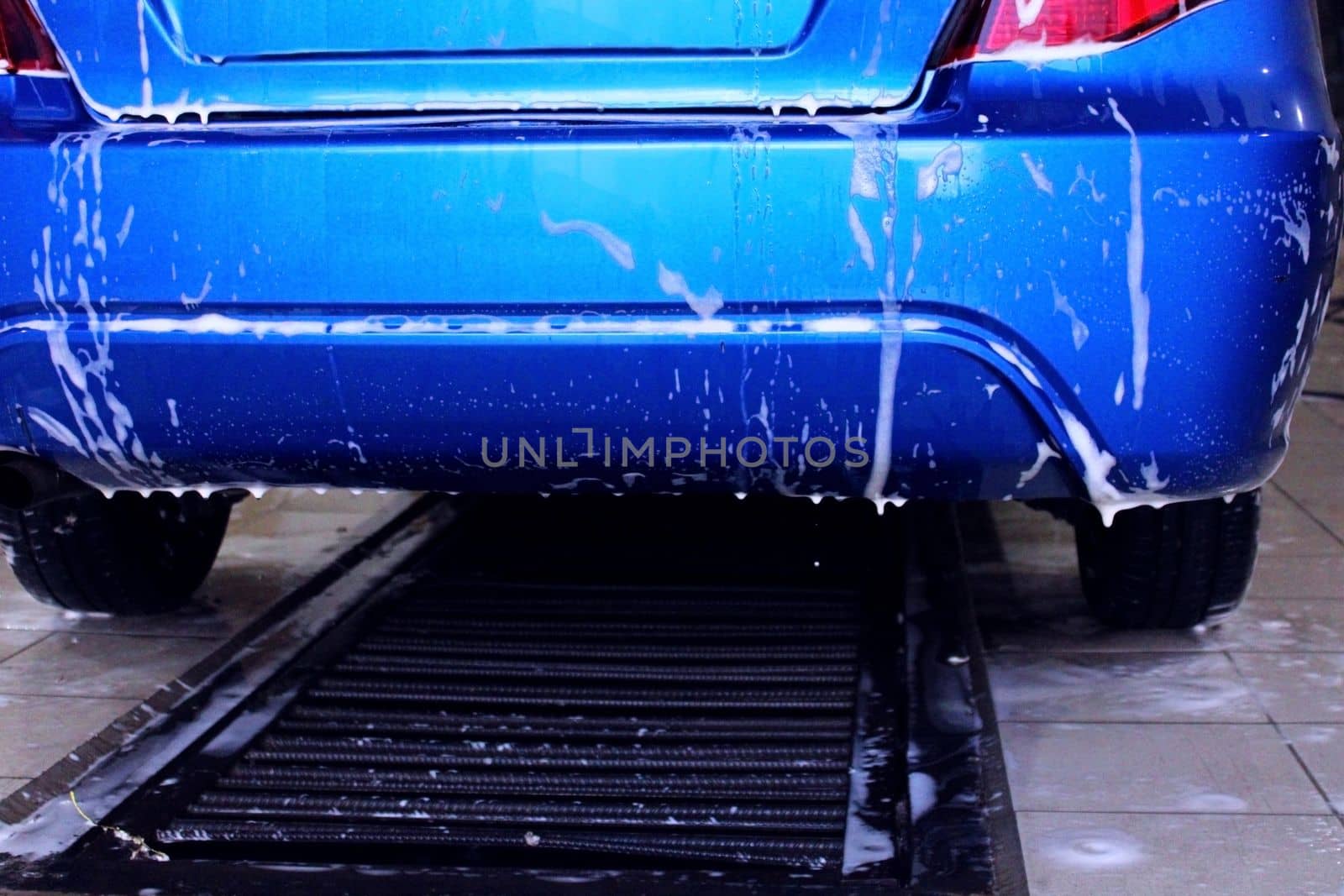 The back of a blue car close-up at a car wash. The concept of ecology and environmental pollution.