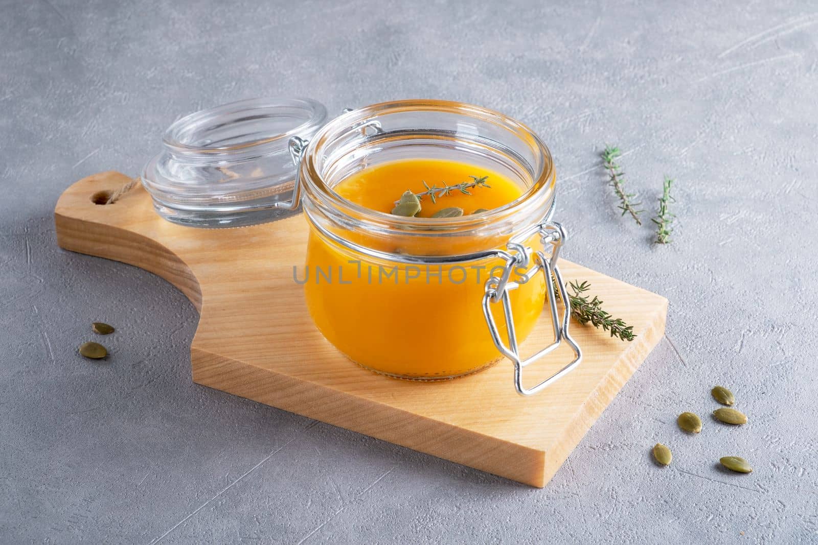 Pumpkin puree soup with pumpkin seeds and thyme in a glass jar on a wooden kitchen board. The concept of healthy nutrition from seasonal vegetables. Selective focus.