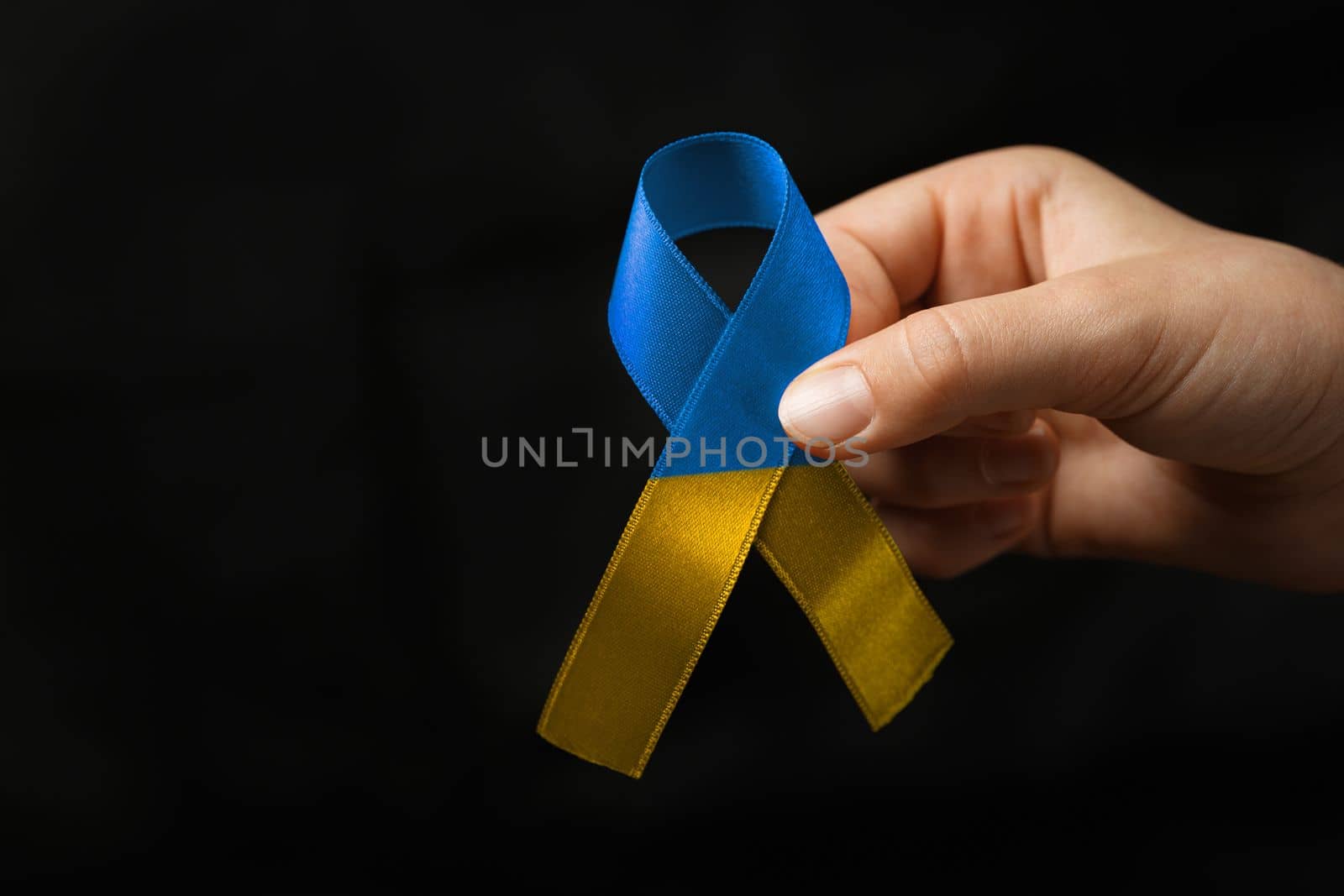 blue and yellow ribbon in female hands on dark background. concept needs help and support, truth will win