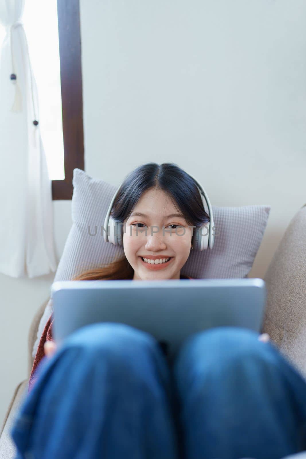 Portrait of asian woman using tablet and headphones relaxing on sofa at home.