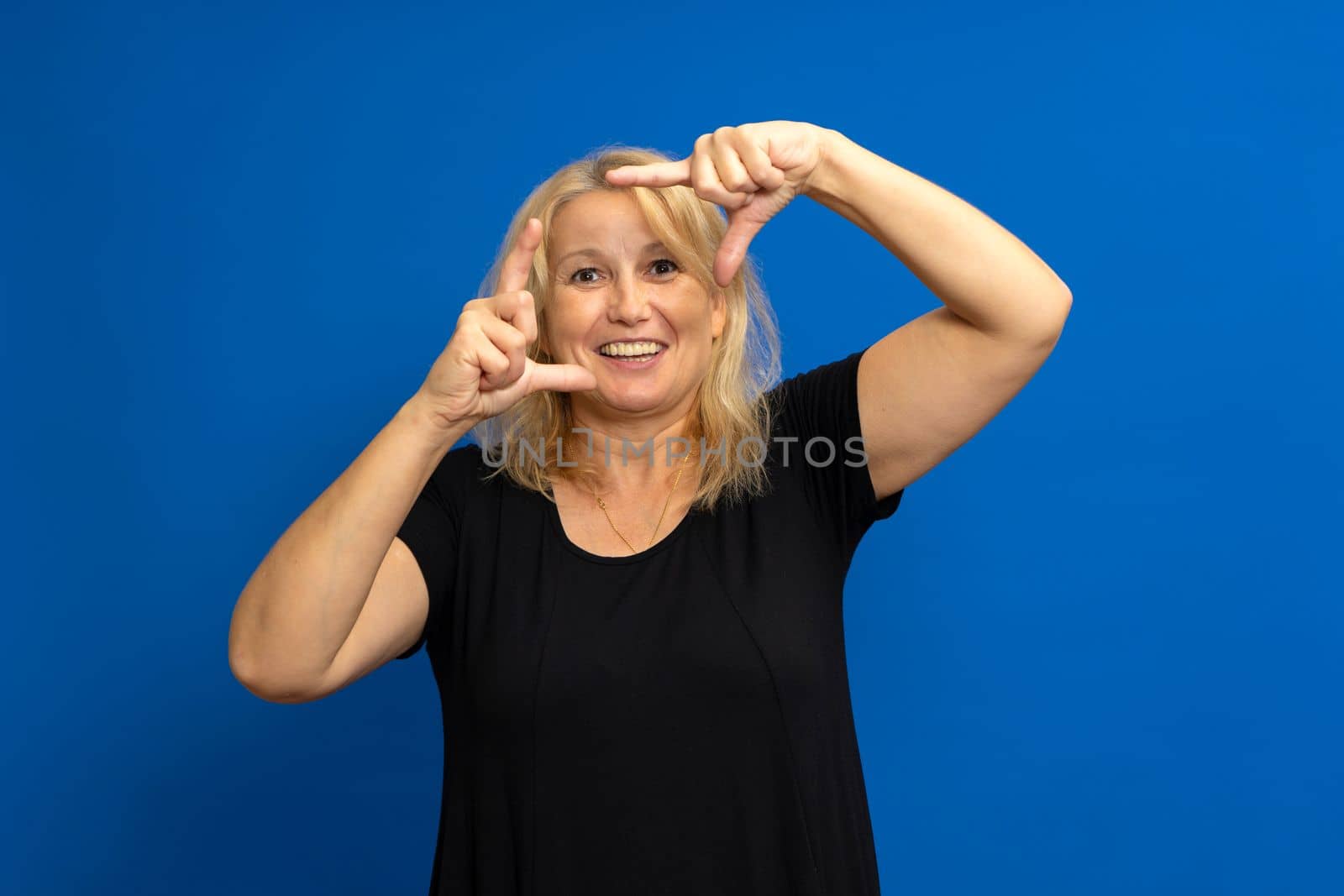 Caucasian happy blonde woman making frame with fingers isolated on a blue background.