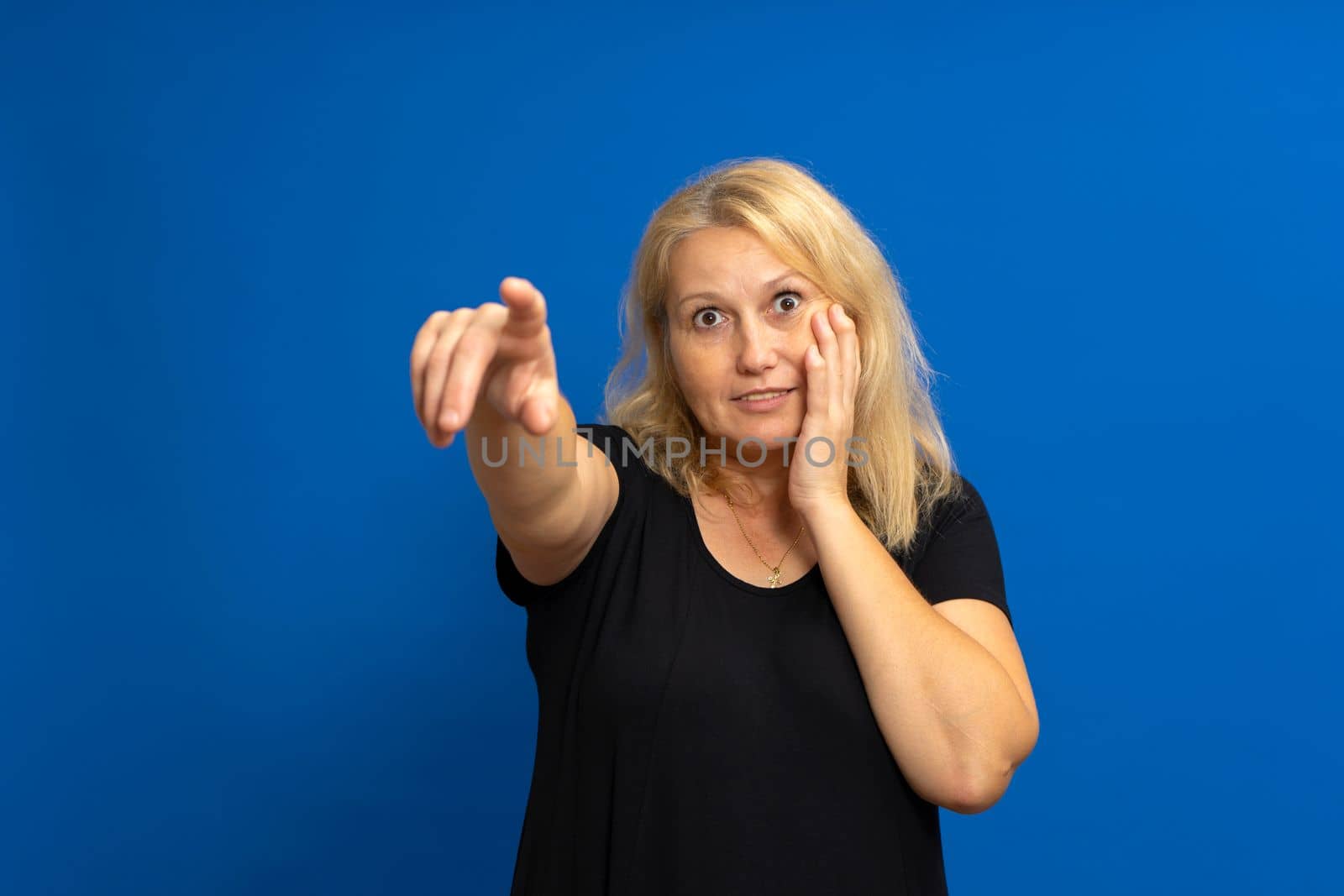 Surprised attractive cute blonde straight-haired caucasian woman in casual black t-shirt pointing finger at the far road. Isolated on blue background