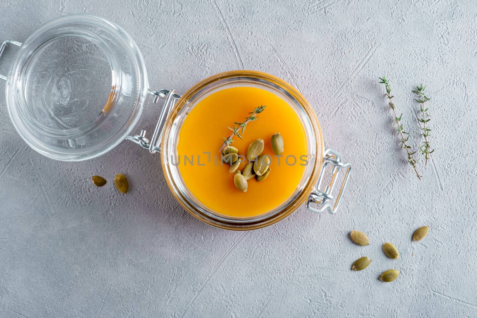 Pumpkin puree soup with pumpkin seeds and thyme in a glass jar. View from above.