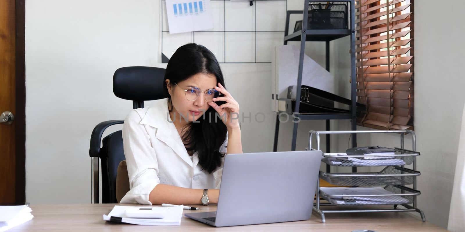 Tired female employee holding head on hand, looking at computer screen, doing hard task, having problem with computer software. Stressed exhausted businesswoman suffering from headache, feeling bored. by wichayada