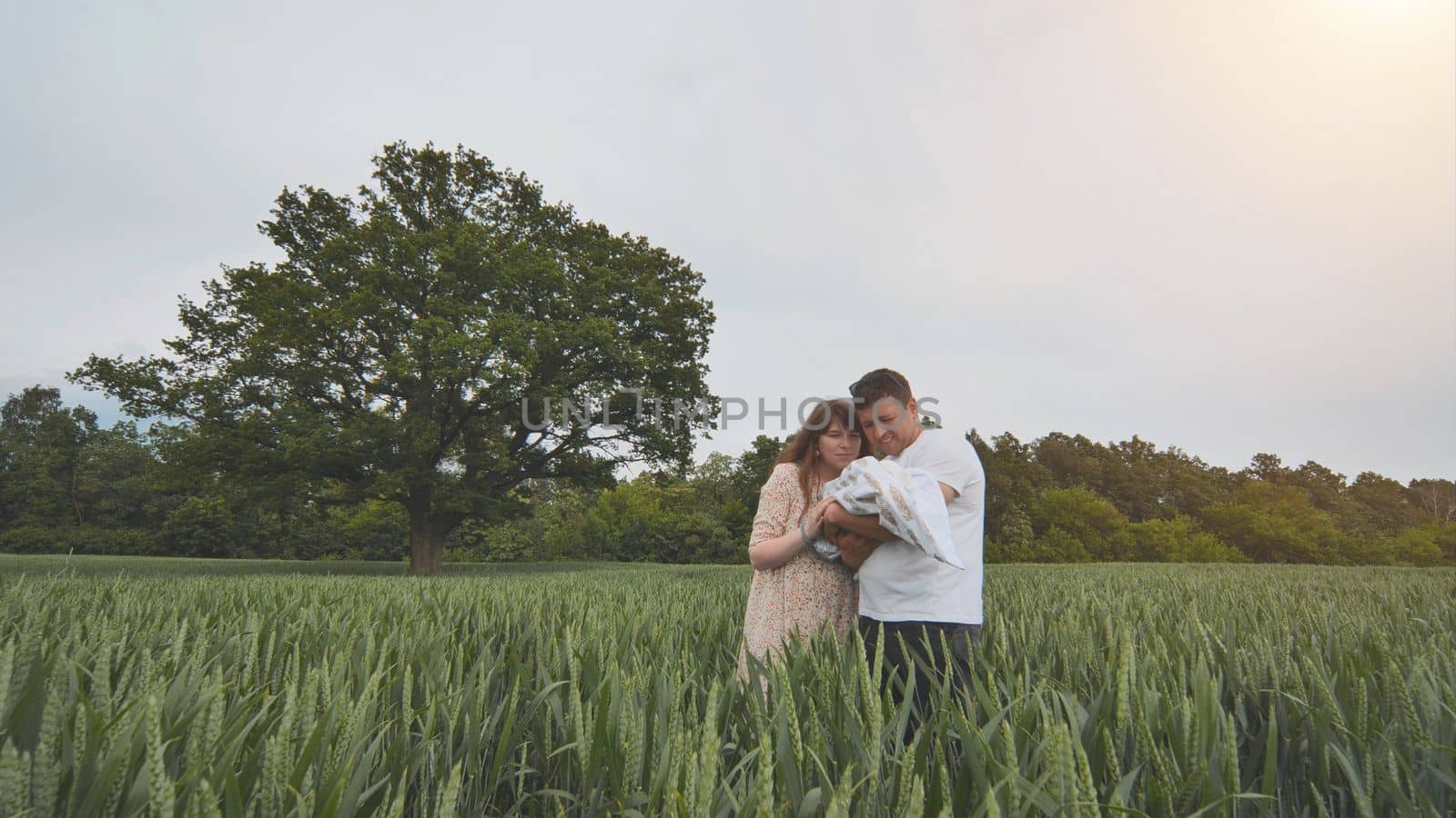 A young couple with their newborn baby in green wheat in a field