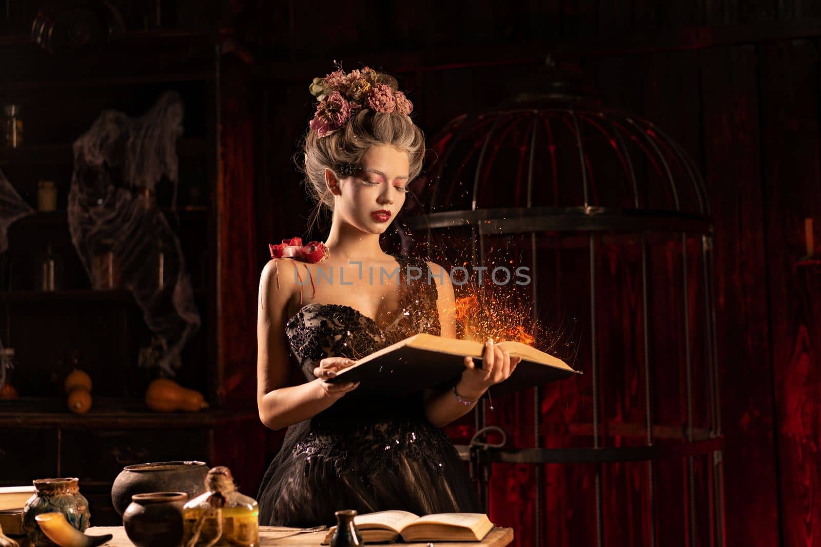 Charming woman witch flowers in hair vintage black dress with book of spell in the old castle. Witchcraft concept, fairy tale mystic atmosphere. Conjure magic spells