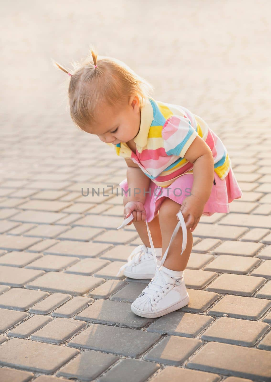 fair-haired baby in tennis clothes ties shoelaces at sunset.