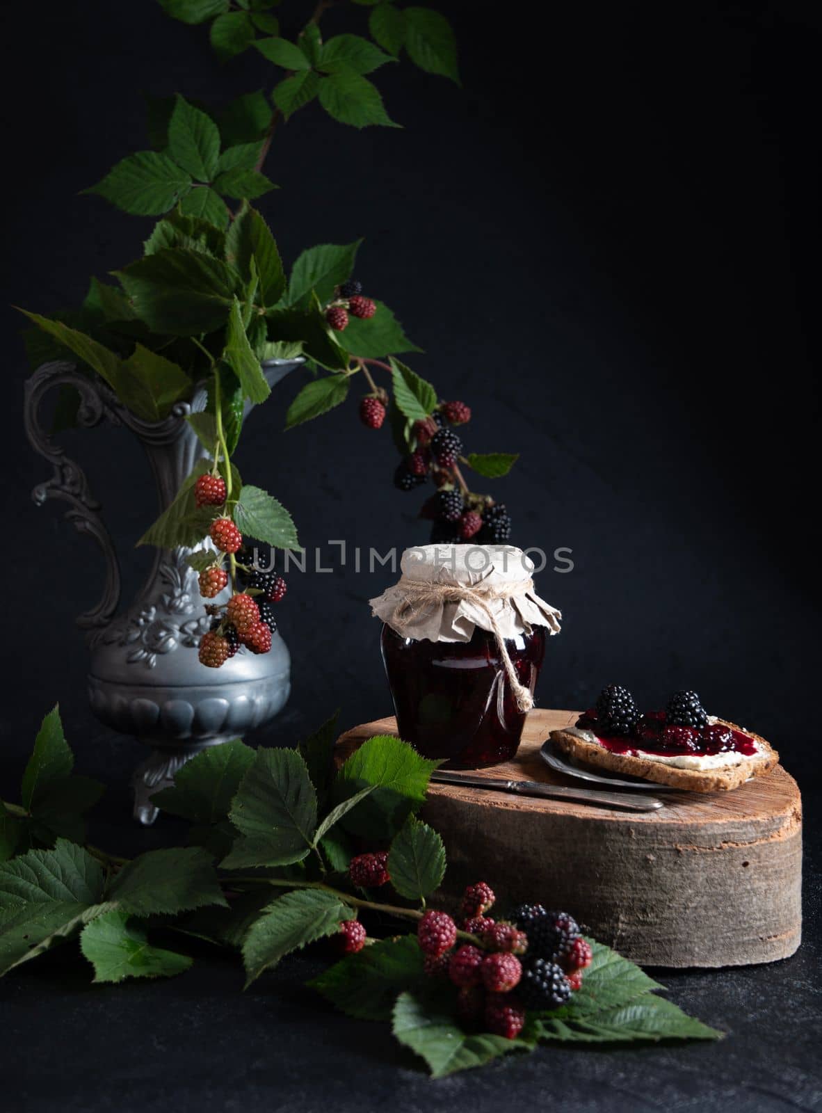 still life with a jar of blackberry jam and bruschettas with soft cheese and berries, decorated with a branch with green leaves, High quality photo