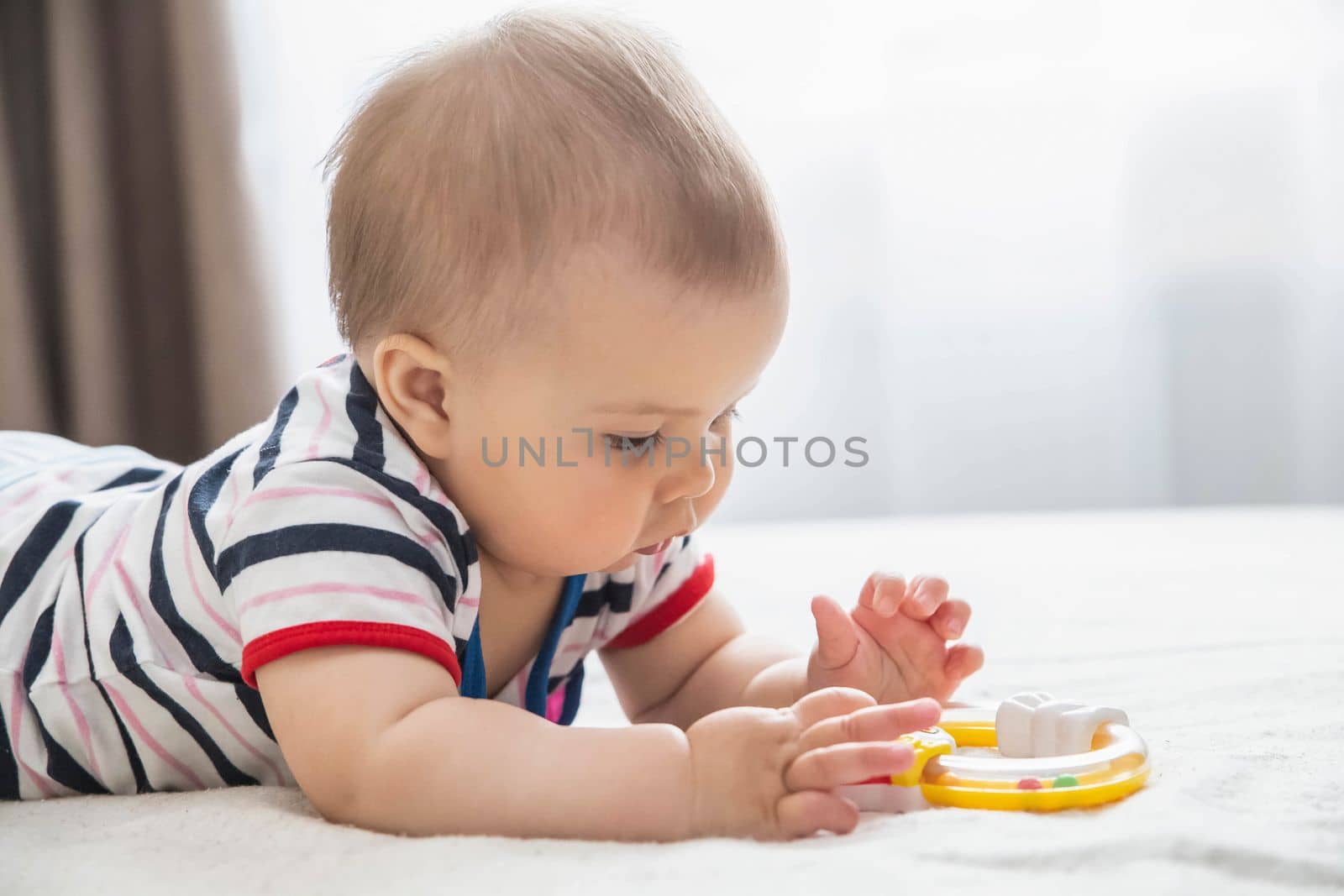 beautiful baby lies on the bed and plays by yellow toy.