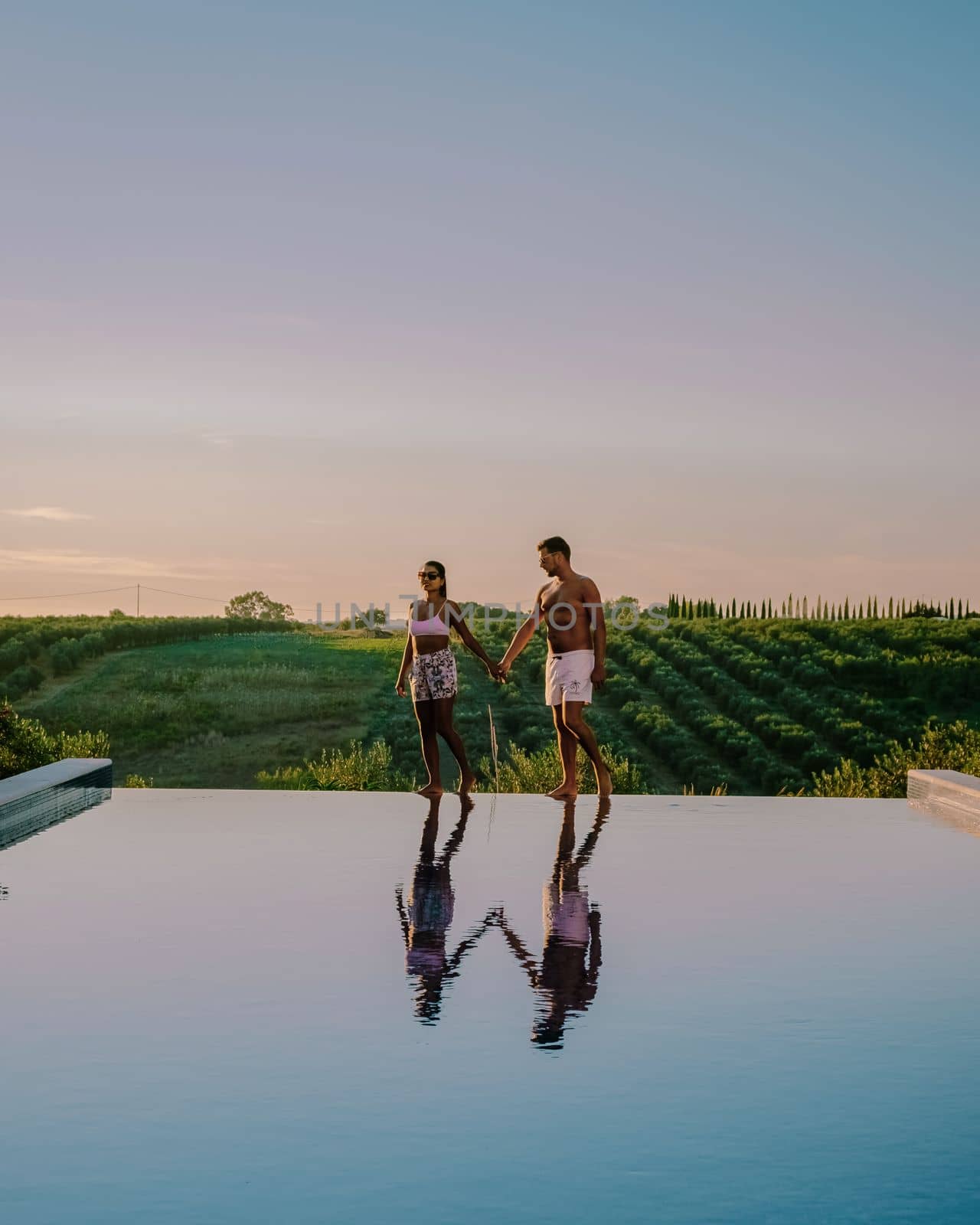 Couple at a Luxury resort swimming pool with a view over wine fields at sunset in Sicily Italy.