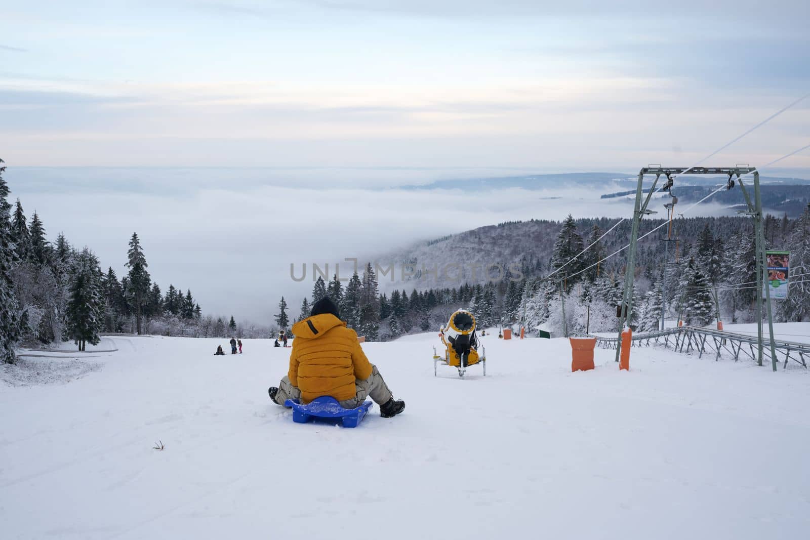 a man rides a sled against the backdrop of a magnificent winter landscape on the Wasserkuppe mountain in Ren, Hesse, Germany. magical tall and large pines and snowy firs covered with snow and ice. The horizon creates an illusion and merges with the cloudy sky and fog, which covers all the space visible in the distance. High quality photo