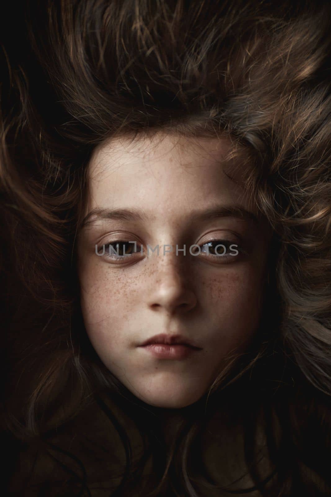 The girl's face appears on a dark hair background. Portrait of a girl shot in the studio. High quality photo