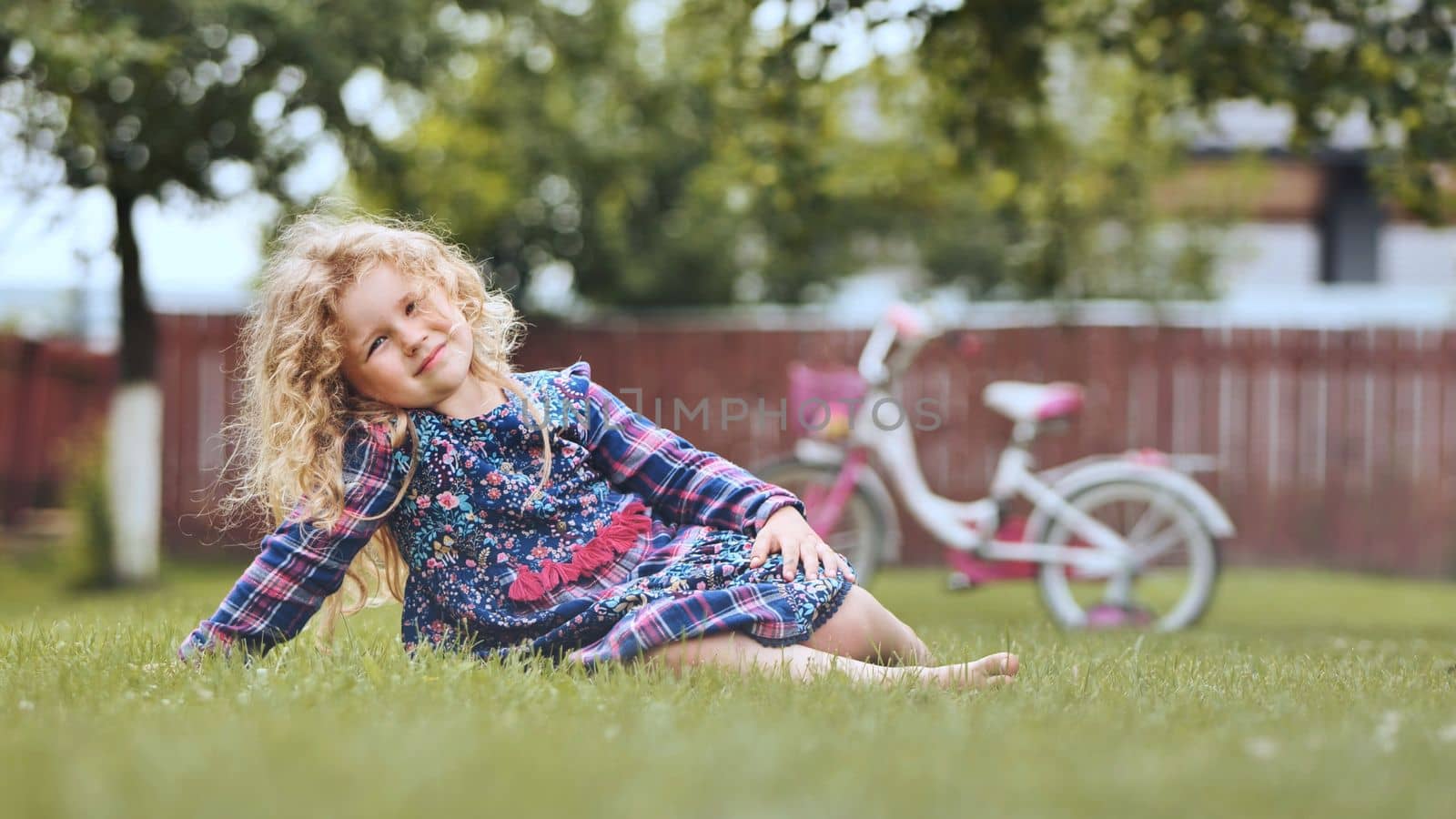 A little girl in the garden on the grass with her bicycle in the background