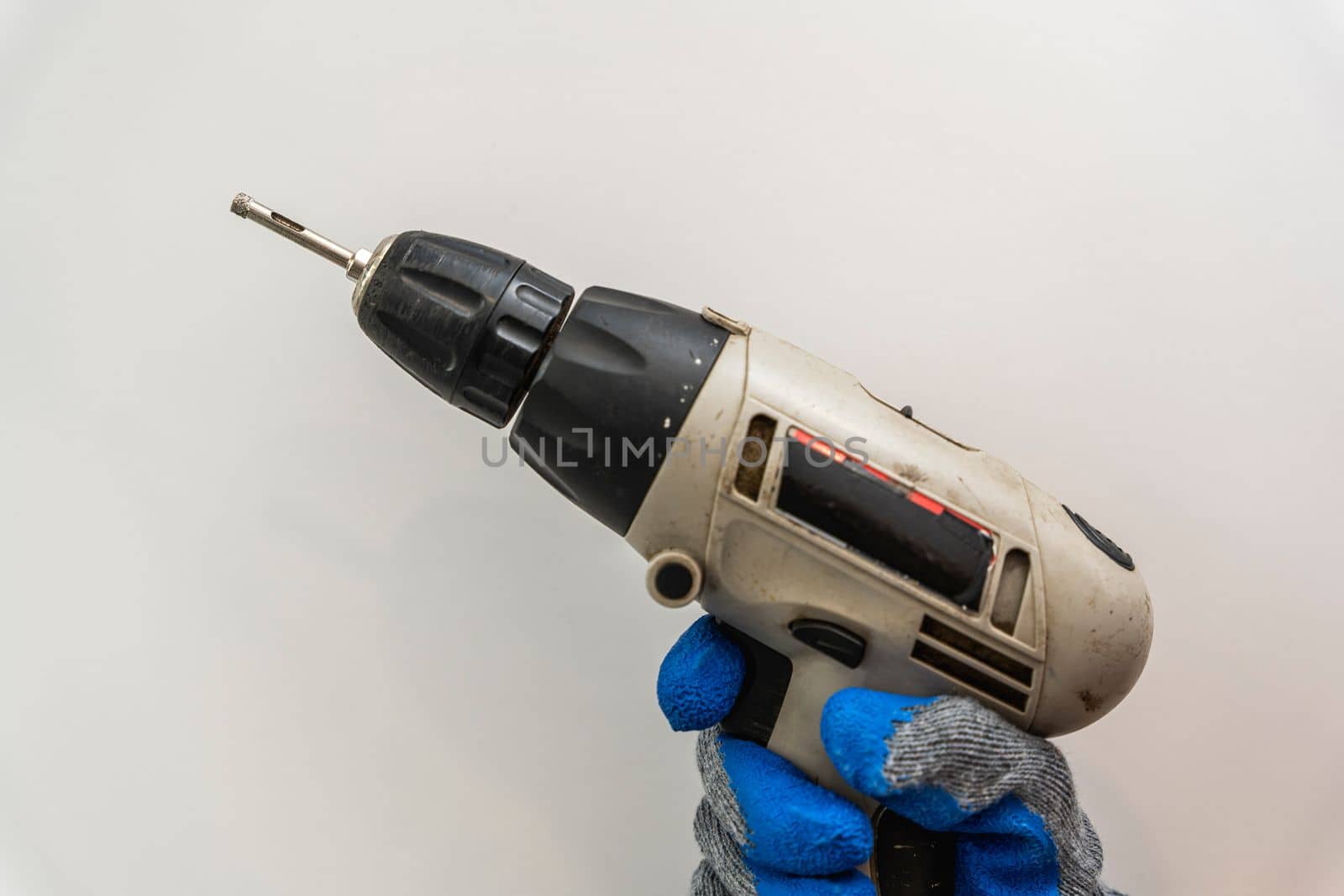 a cordless screwdriver in the hands of a man in work gloves on a white background.