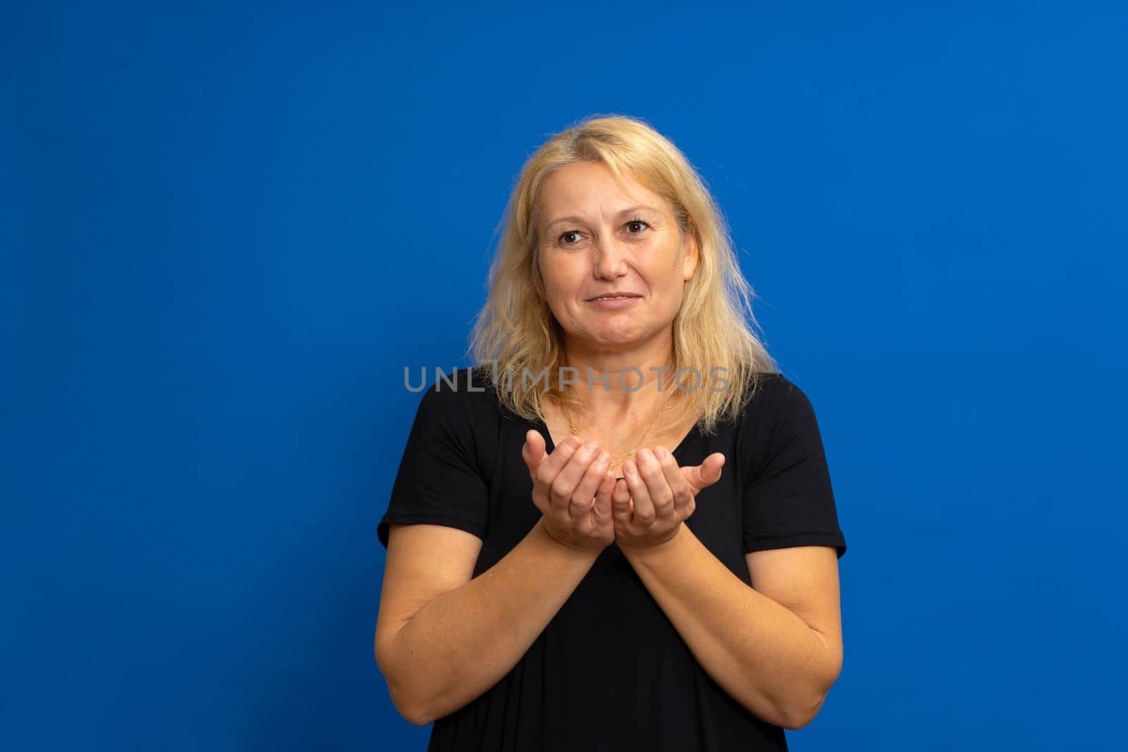 Closeup portrait of a smiling, happy excited beautiful woman with raised palms arms in you offering something, isolated over blue background. Positive emotion facial expression sign symbols