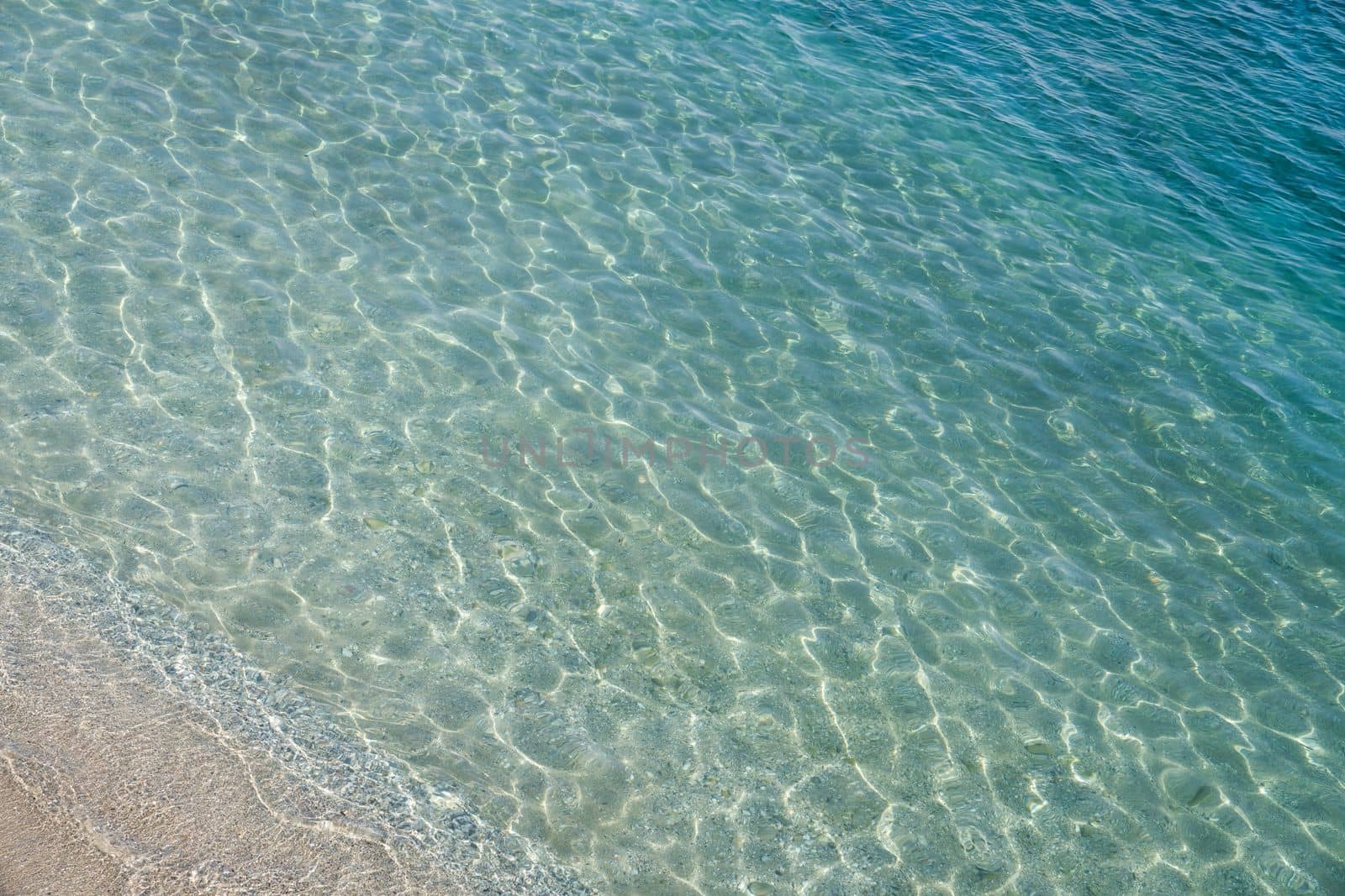 Sandy beach that goes under sea surface of water. Beautiful gradient of pale blue color. Sun glare on water surface