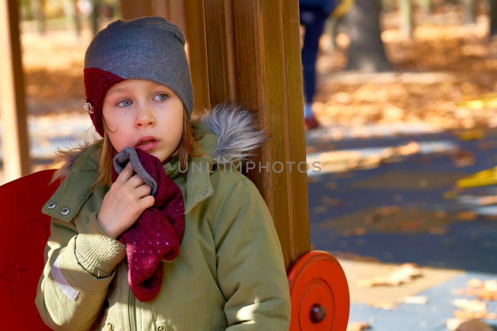 Offended frightened child in a jacket and a hat on an autumn playground by jovani68