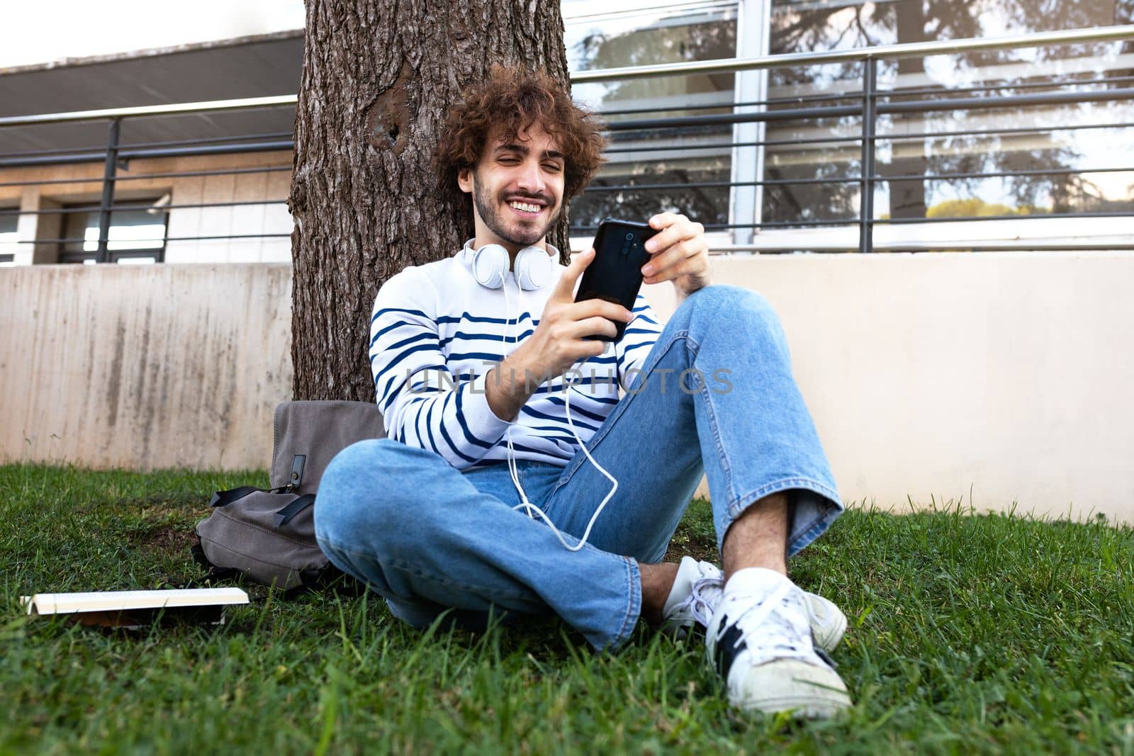 Young man relaxing outdoors using phone in park. Male college student relaxing on campus. Education concept.