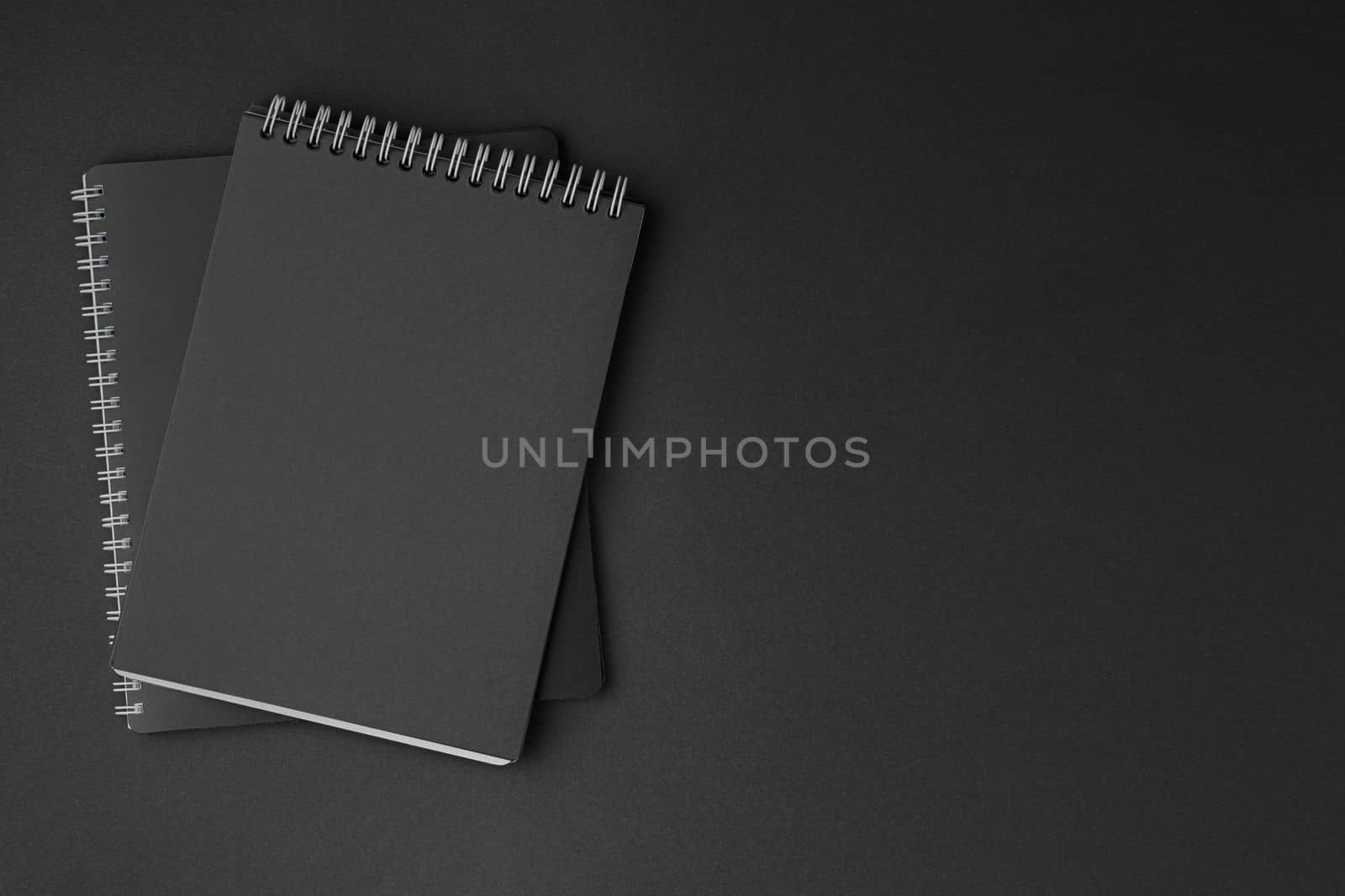 Black notebook with white spiral on dark isolated background. White and black concept flat lay.