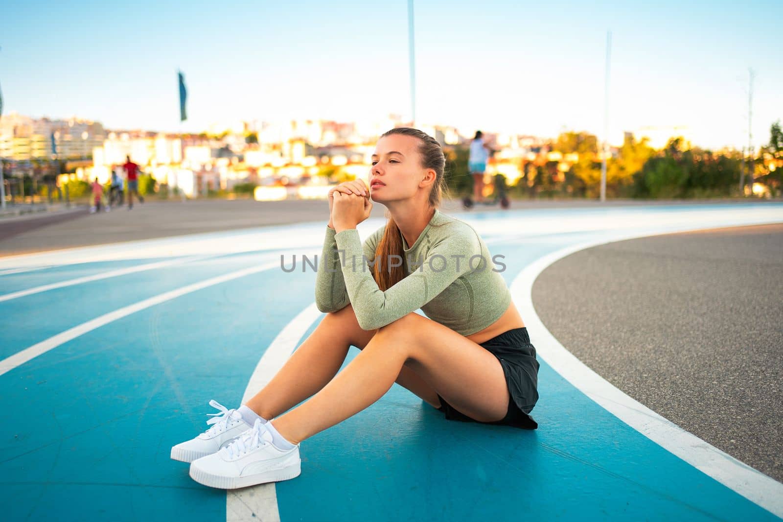 Tired upset female athlete sitting on running track resting after jogging exercises. Disappointed sport result. Amateur sprinter sportswoman exhausted after tough trainings sitting on track