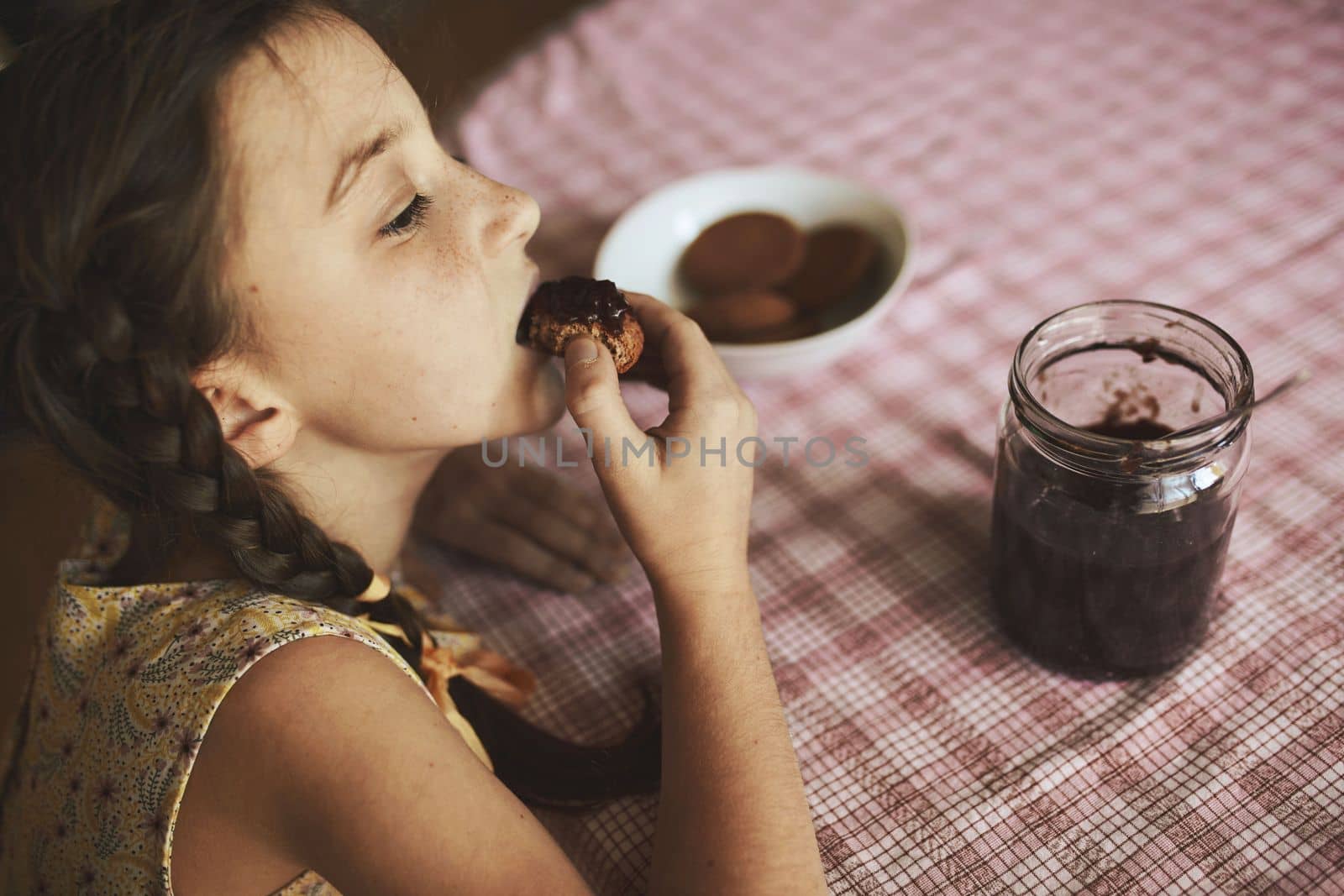 Cute funny toddler girl eats sweet bun for breakfast. Happy child eating bread roll with strawberry jam. Health food for children and kids with selfmade jelly. High quality photo