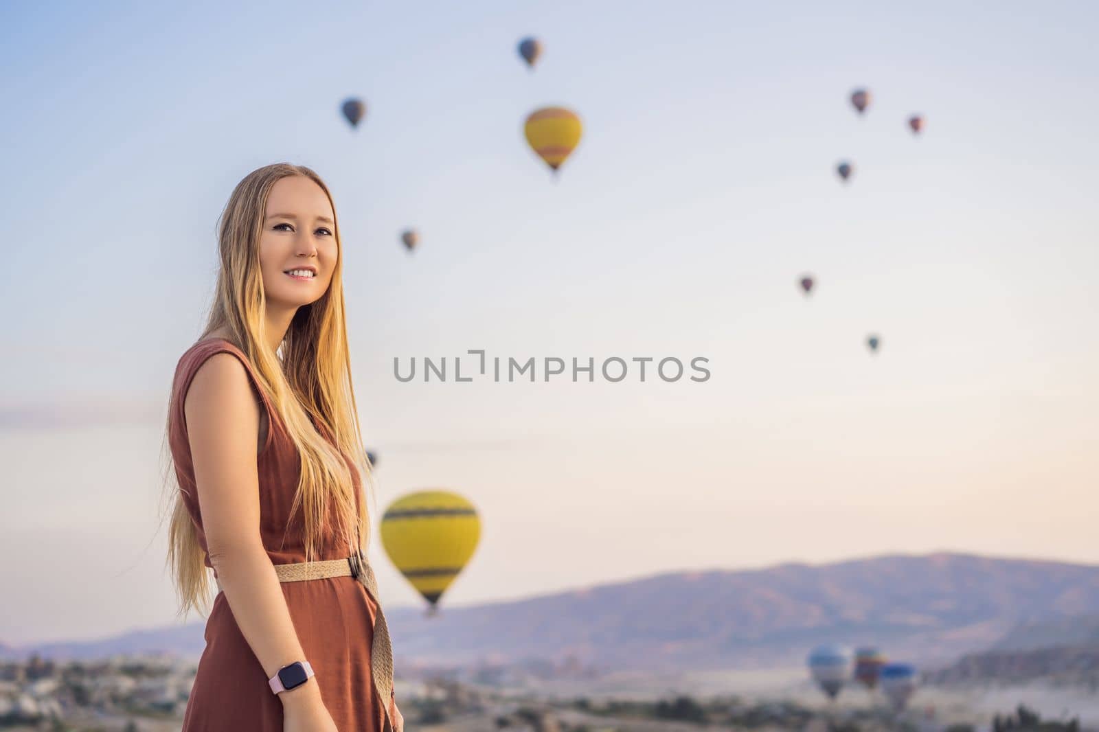 Tourist woman looking at hot air balloons in Cappadocia, Turkey. Happy Travel in Turkey concept. Woman on a mountain top enjoying wonderful view.