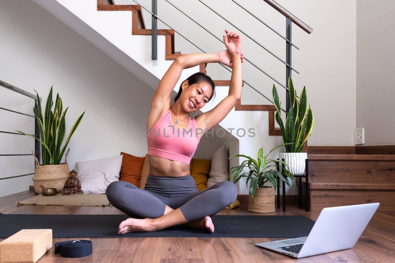 Young Asian woman doing stretching exercises at home following online fitness video with laptop. Doing yoga side bend stretch with tutorial at home. Fitness concept.