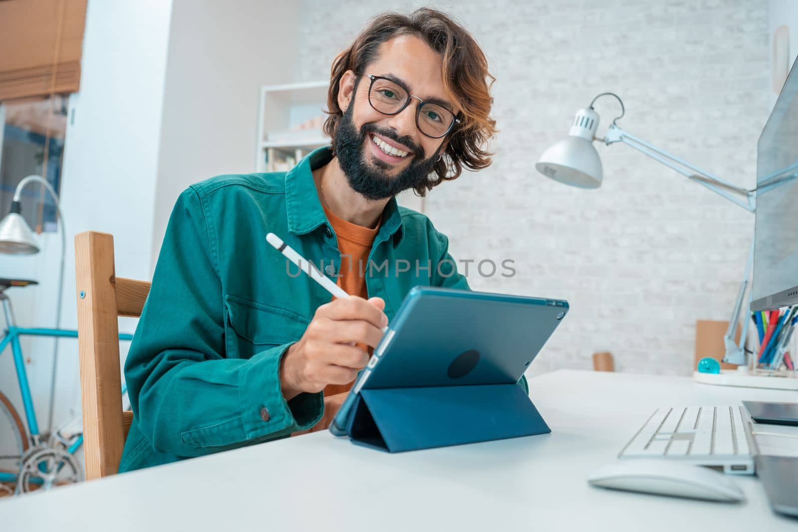 Young designer looking at camera while working with graphics tablet and laptop. High quality photo