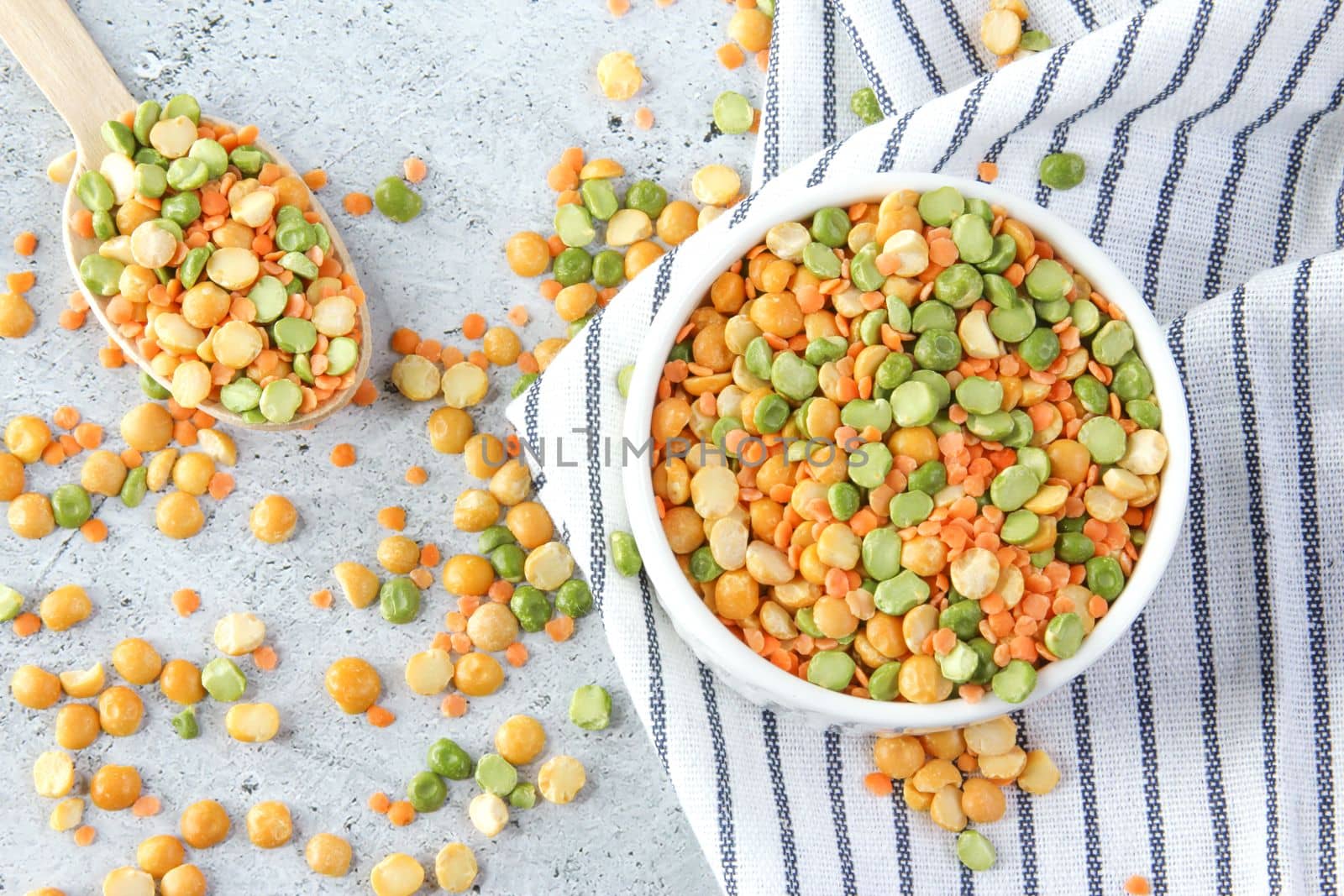 Different types of peas yellow and green in white bowl on a napkin and a light gray stone background, close up, top view.