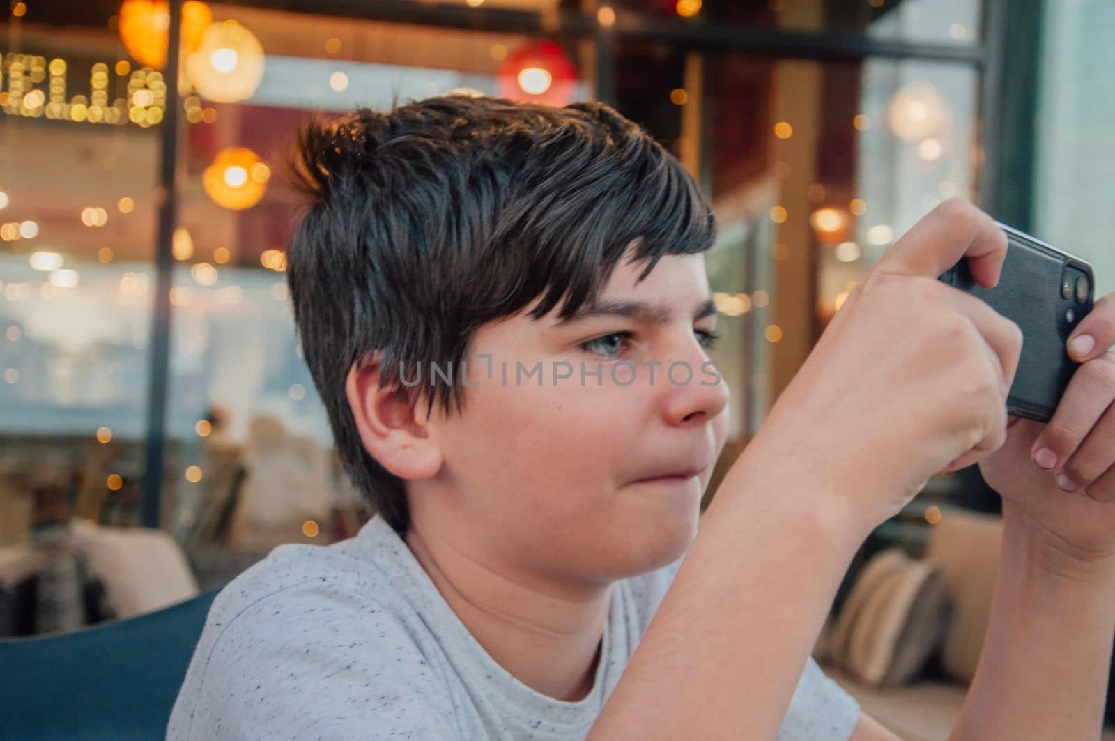 Portrait of young boy playing mobile phone games in a bar, with concentrated expression.