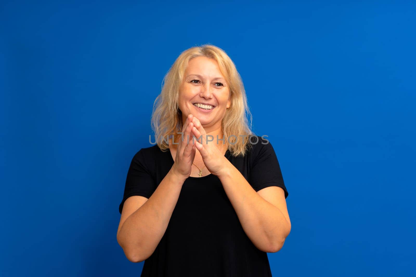 Anticipation of something good idea with a beautiful caucasian woman rubbing her hands together. She is standing on a blue background with copy space. Interesting offer or sale concept.