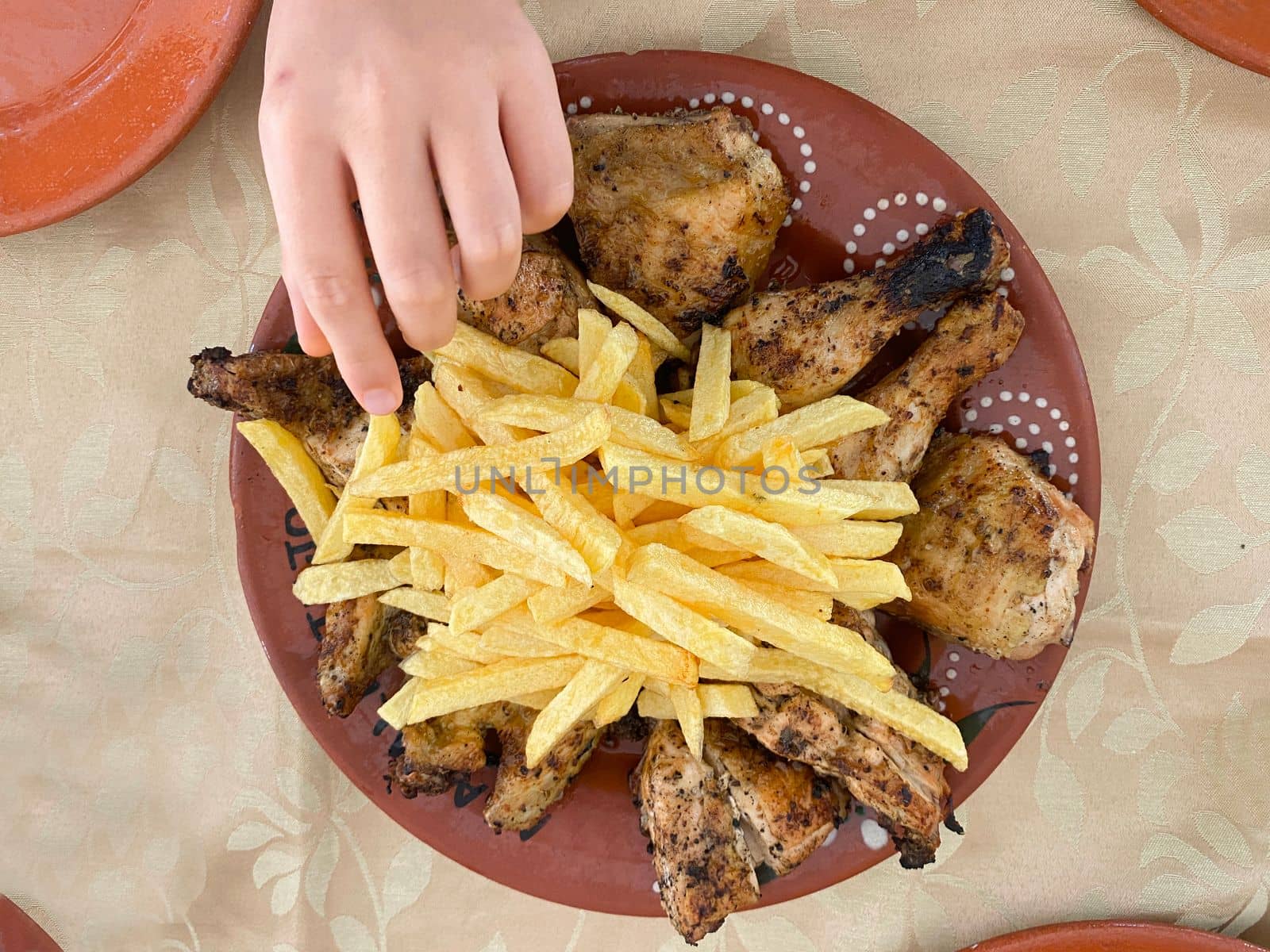 hand picking up food from grilled chicken and french fries plate.