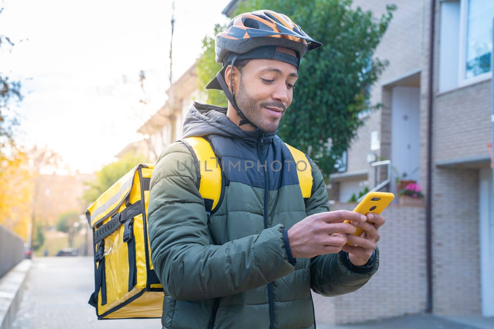 Food delivery concept. Young African American driver with backpack looking smart phone to deliver products for customers who order online purchases. Black male smiling happy with his job.