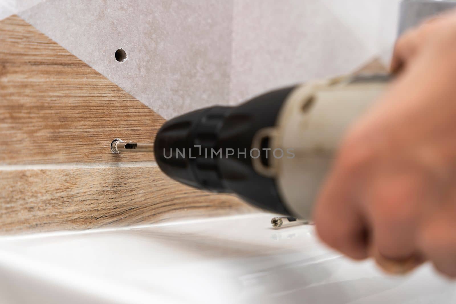 drilling holes in porcelain stoneware, drilling holes in tiles. Close-up of drilling a hole with a special cooled drill in a ceramic tile in the bathroom. a worker in the bathroom drills holes in the porcelain tile with a drill to install shelves. home renovation.