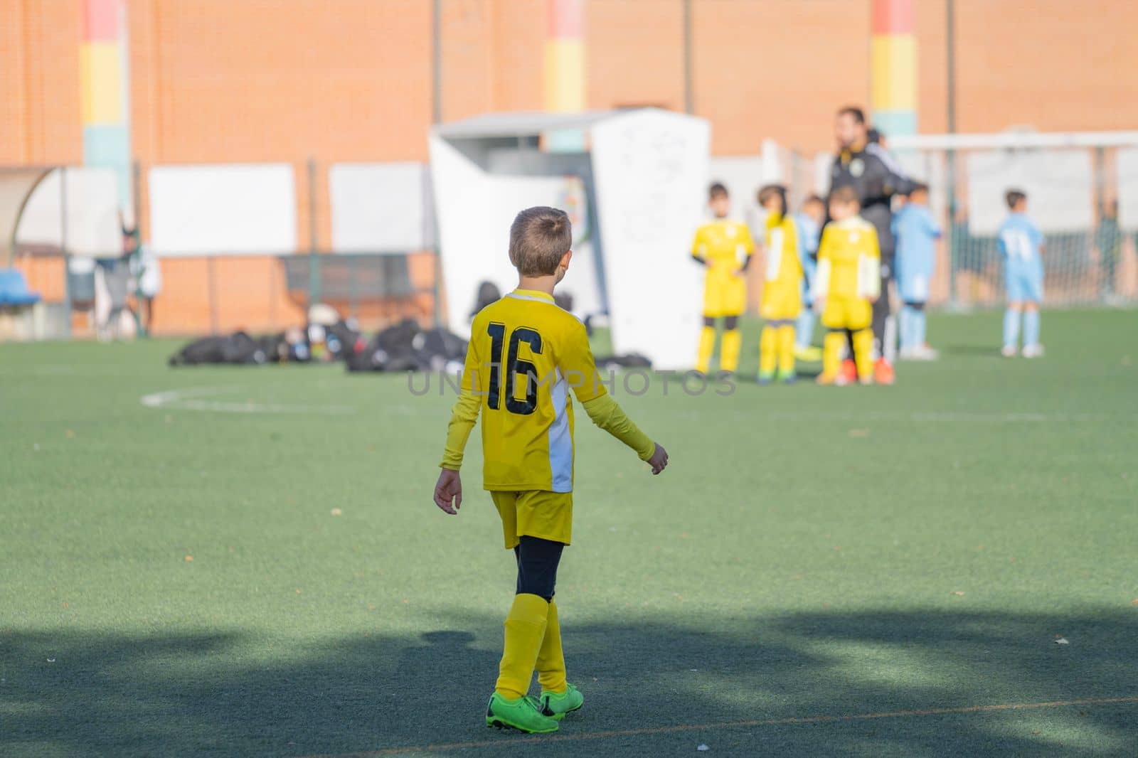 Rear view of Kid football player alone looking bench and coach on a competition match.