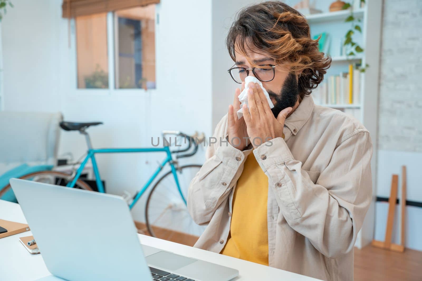 Ill at work young man got flu allergy sneezing blowing wiping running nose in tissue - allergic guy caught cold at job sitting at home office workplace having respiratory disease sick leave concept. High quality photo