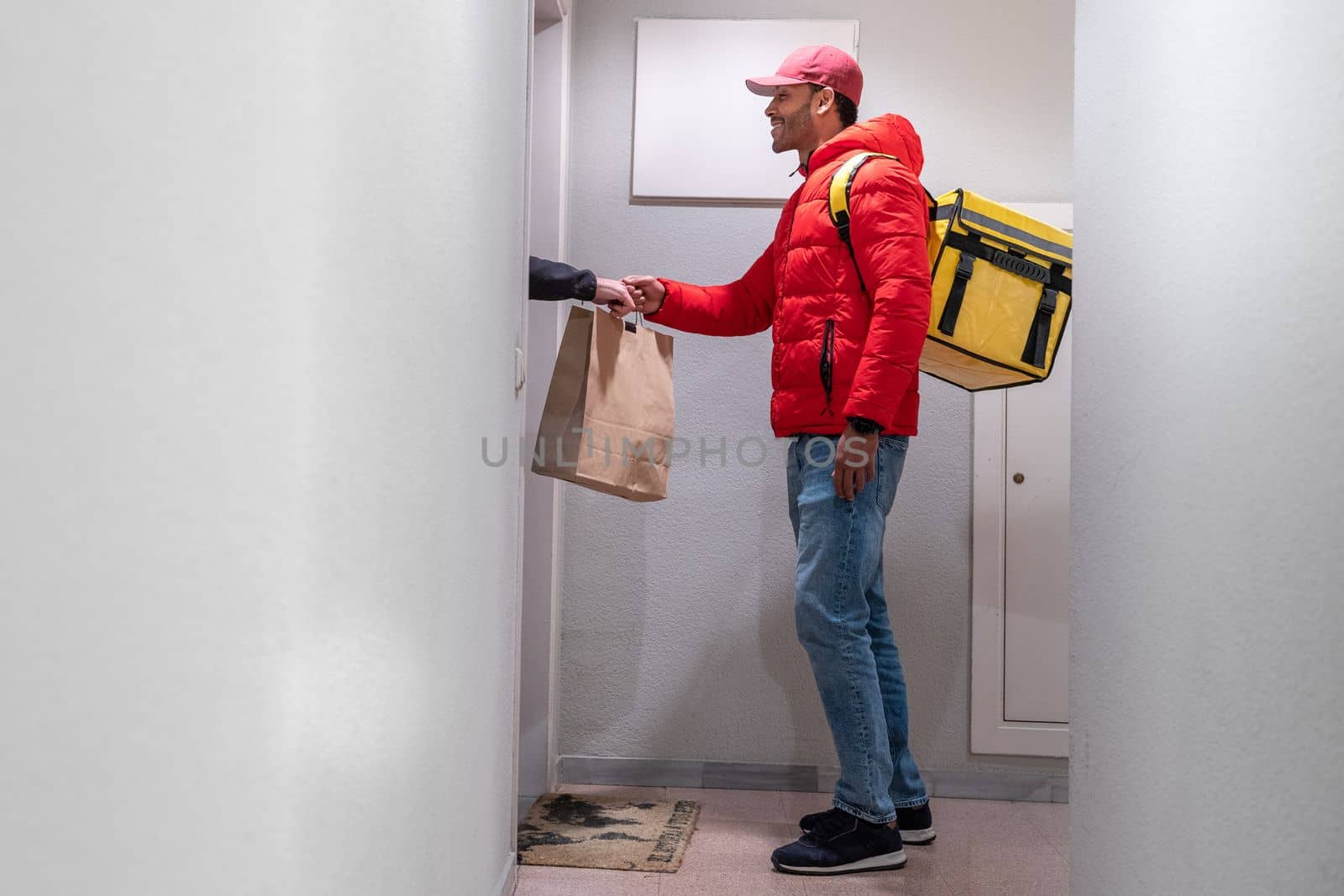 Food delivery concept. Young smiling African American with backpack delivering products at door. by PaulCarr