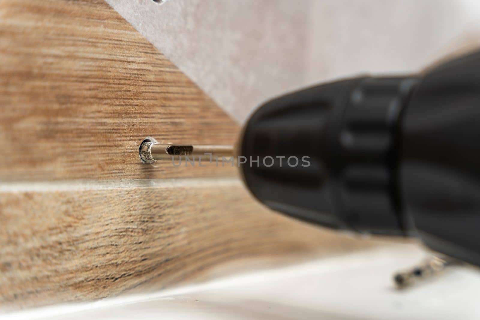 drilling holes in porcelain stoneware, drilling holes in tiles. Close-up of drilling a hole with a special cooled drill in a ceramic tile in the bathroom. a worker in the bathroom drills holes in the porcelain tile with a drill to install shelves. home renovation.