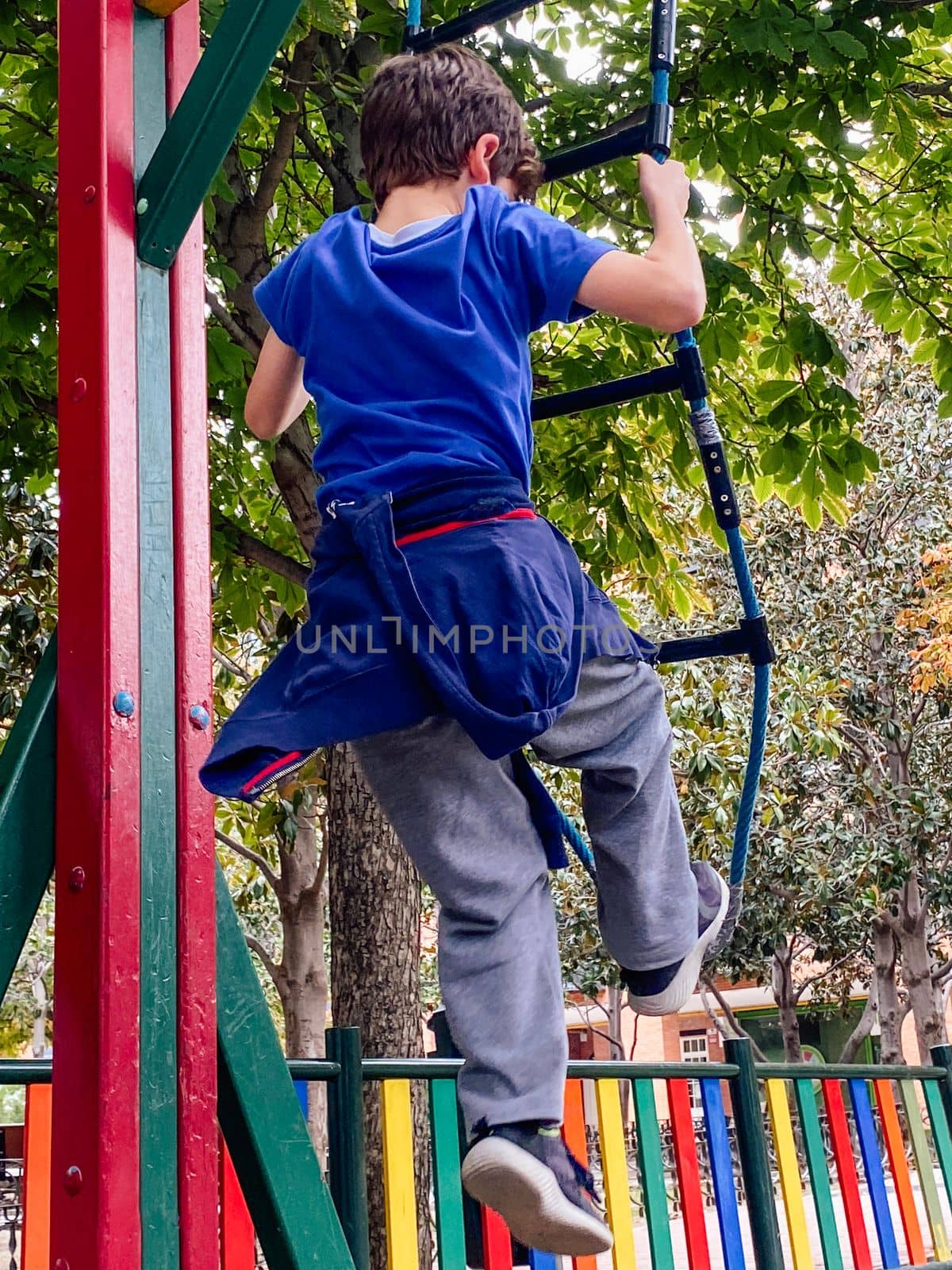 Rear view of child boy climbing on the rope ladder in a park playground.