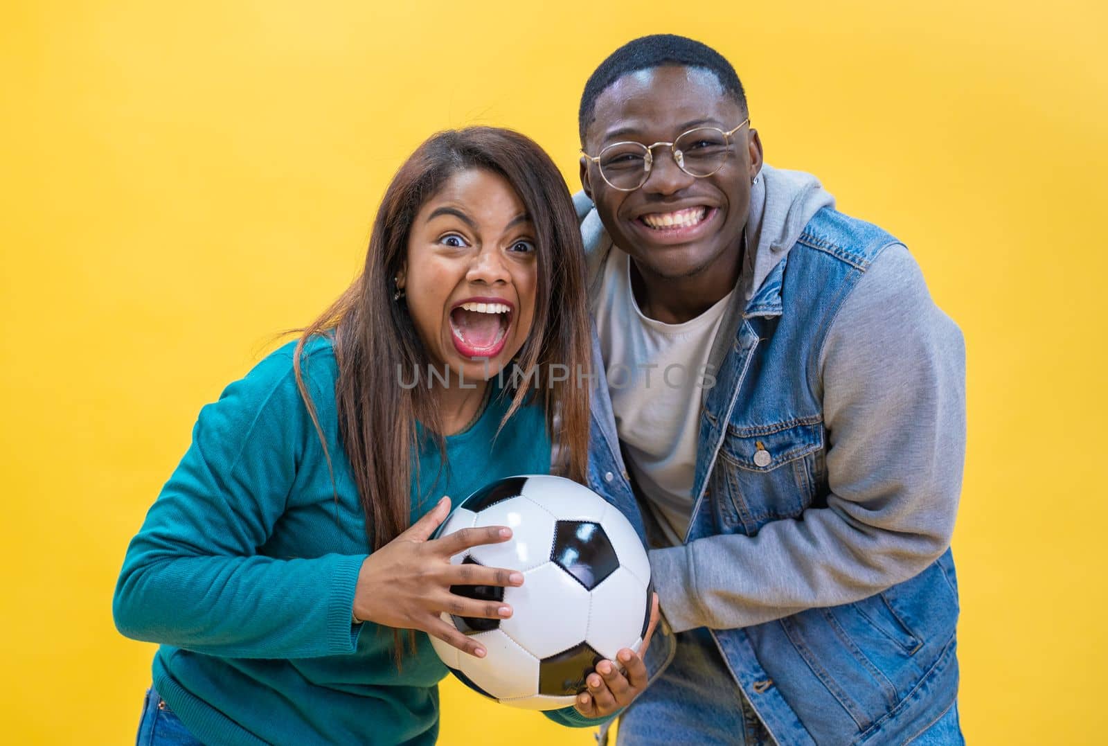 Excited ethnic diversity couple enjoying soccer together isolated on yellow background happy. by PaulCarr