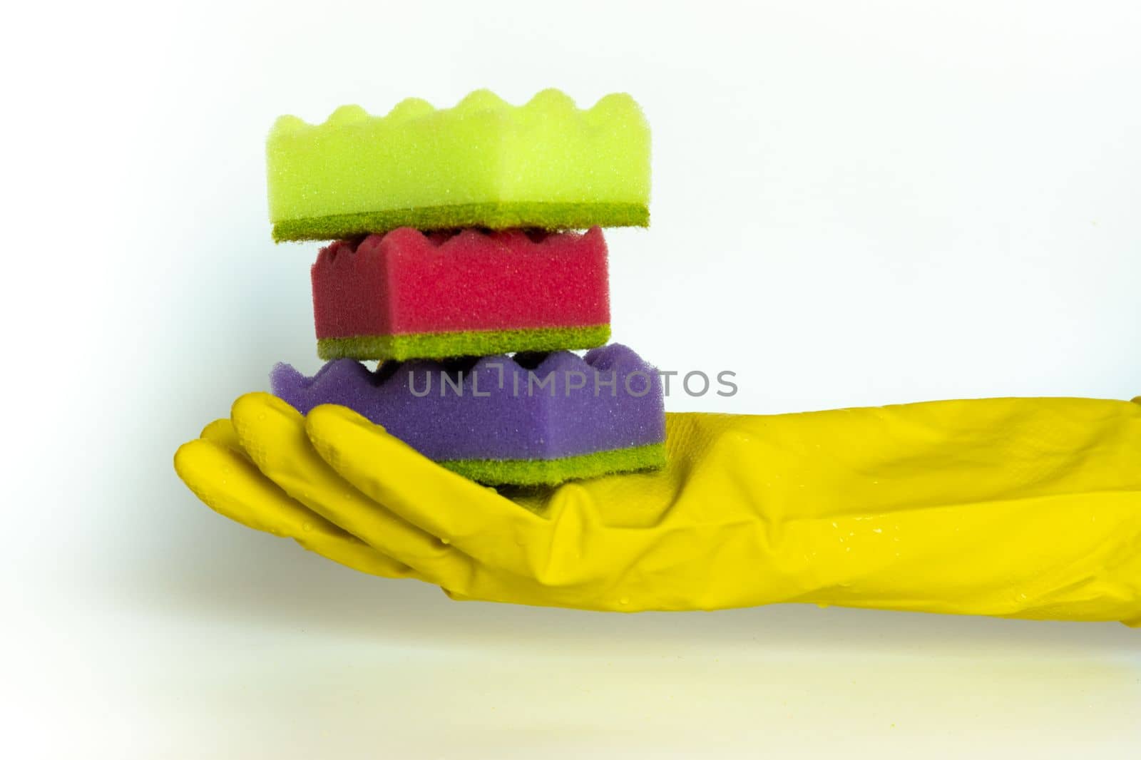 Stack of vivid multi-colored dish wash sponges in woman hand in protective glove. Household cleaning scrub pad. Home cleaning concept. Space for text.