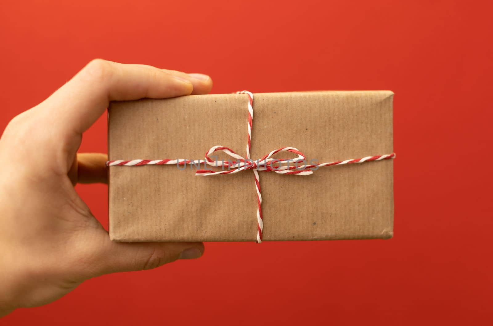 hand holding craft wrapped gift over red background by Chechotkin