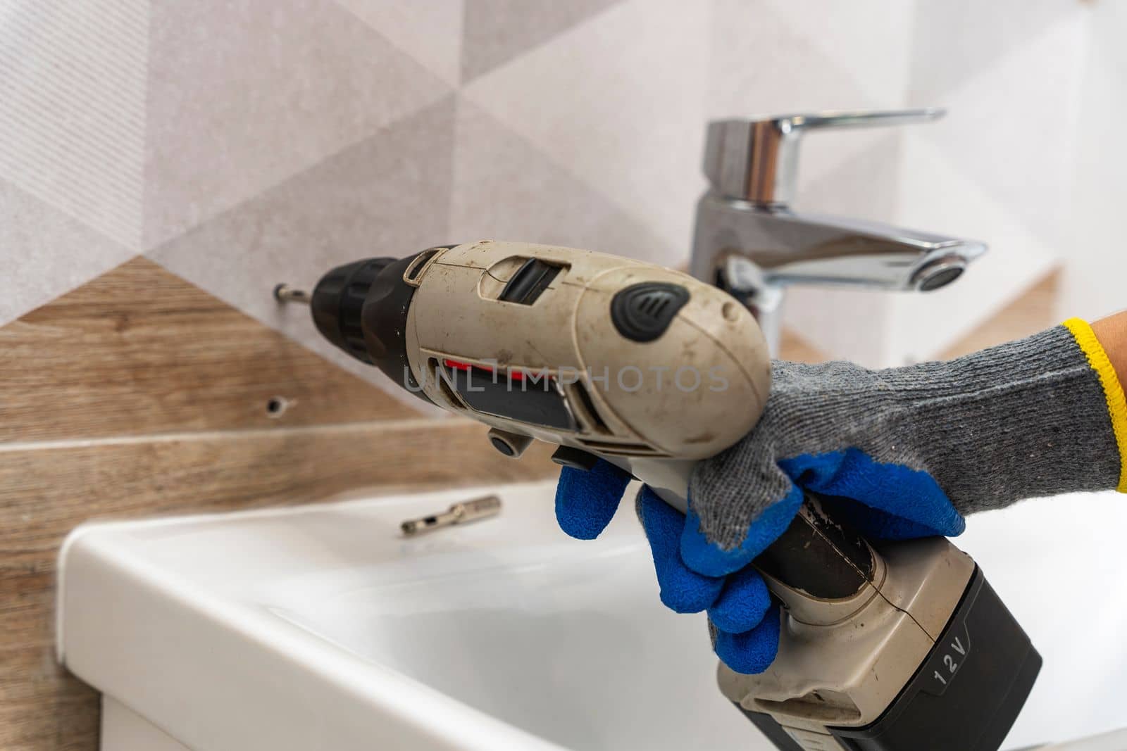 drilling holes in porcelain stoneware, drilling holes in tiles. Close-up of drilling a hole with a special cooled drill in a ceramic tile in the bathroom. a worker in the bathroom drills holes in the porcelain tile with a drill to install shelves. home renovation.