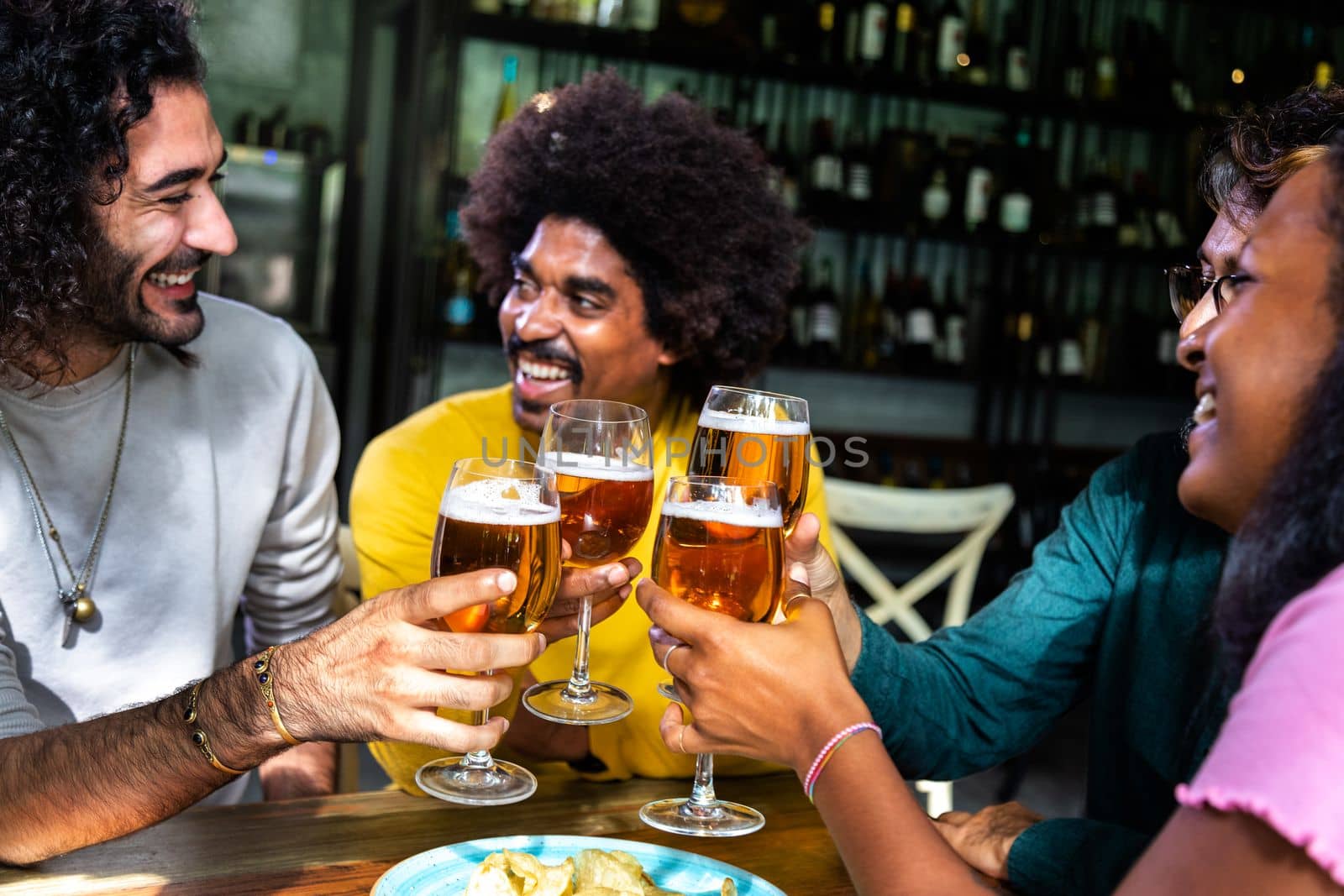 Multiracial happy friends enjoying drinks at a bar toasting, celebrating with beer. by Hoverstock