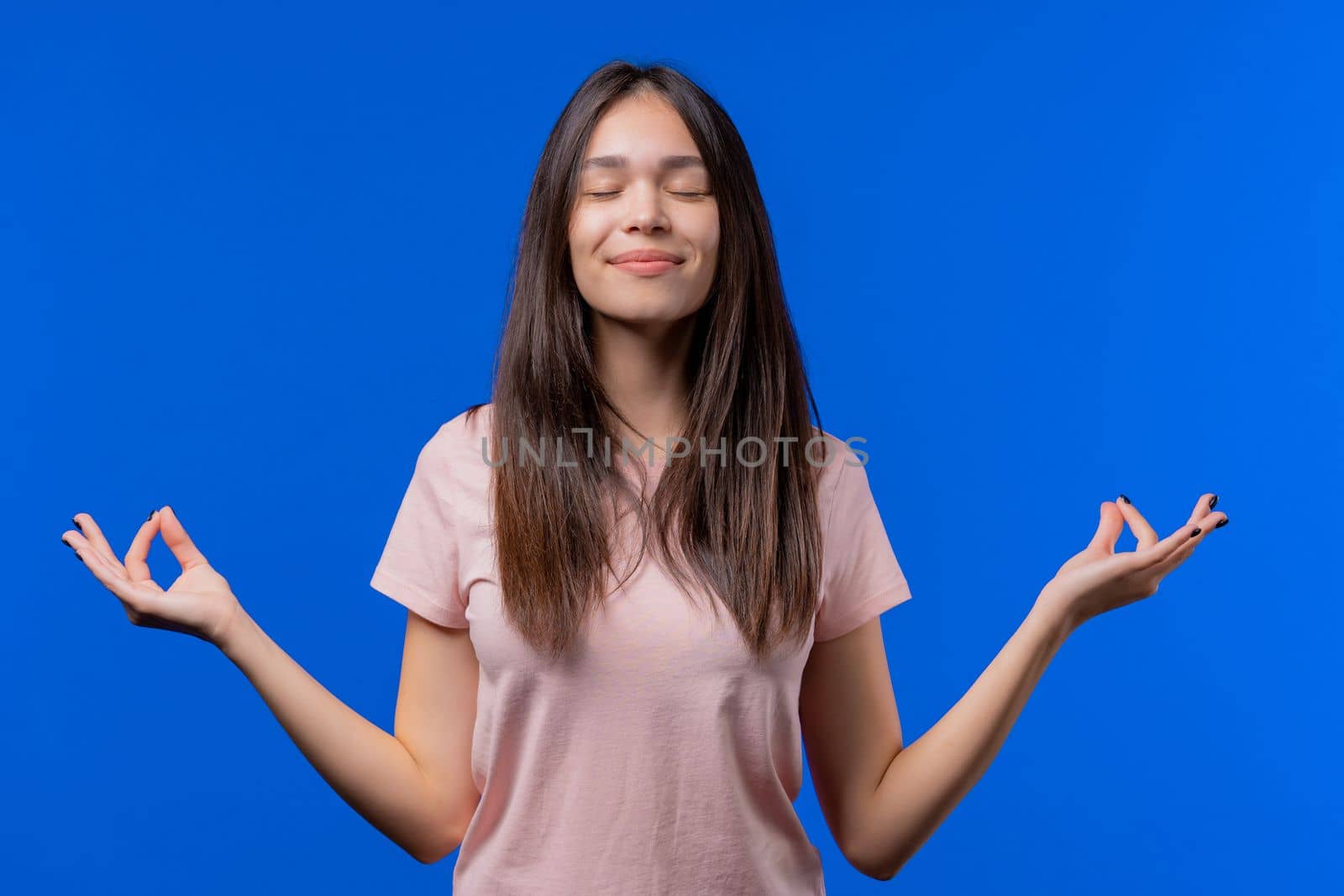 Calm woman relaxing, meditating, refuses stress. Young teen girl breathes deeply, calms down blue studio background. Yoga, moral balance, zen concept. High quality photo